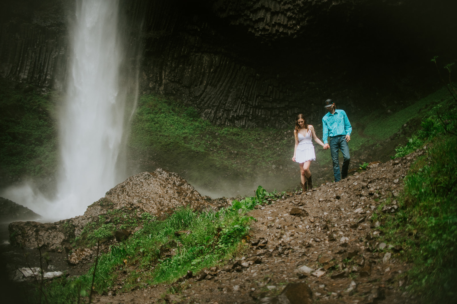 Couple walking along rocky trail near waterfall, adventurous outdoor engagement photos