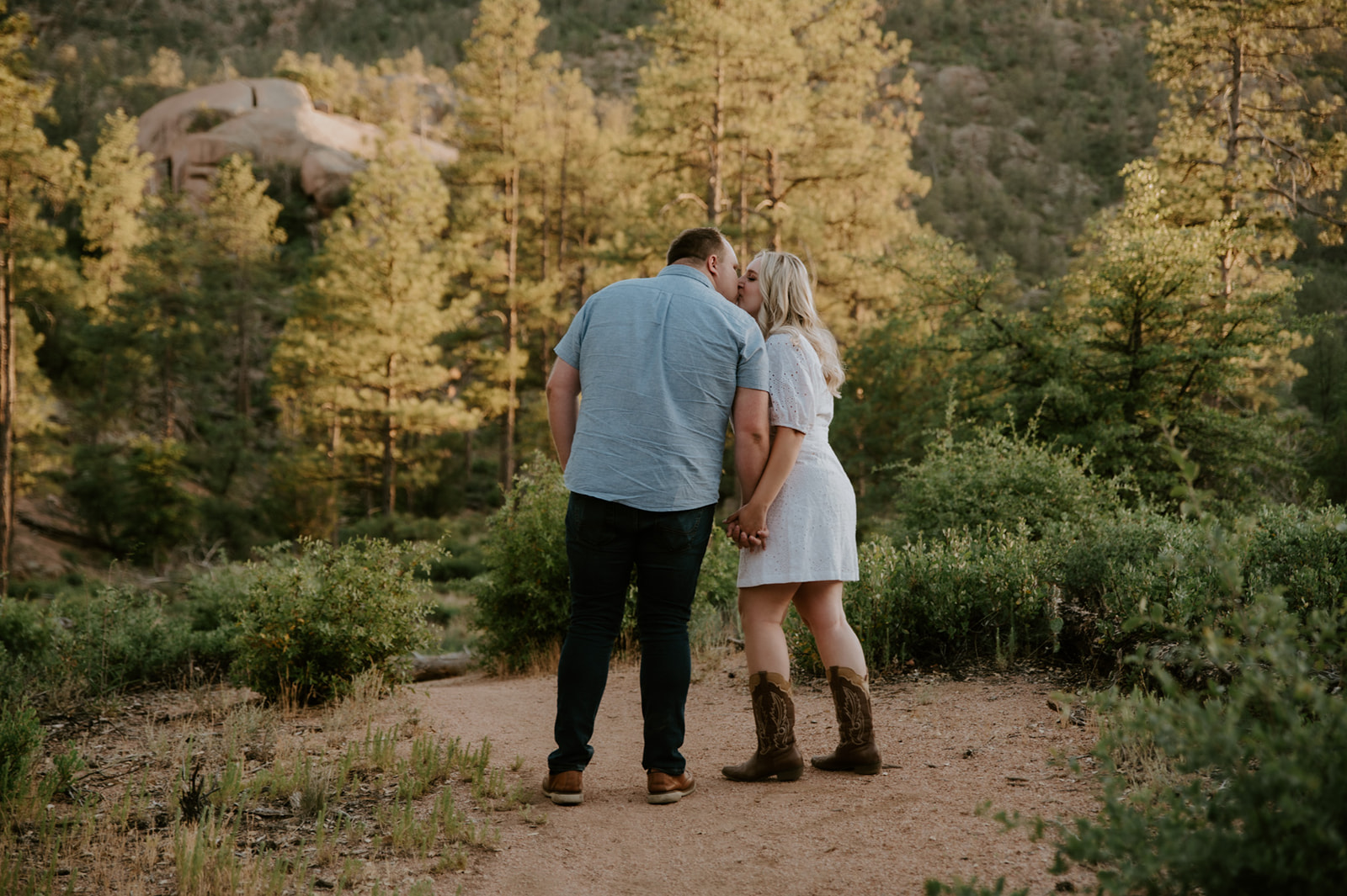 Couple holding hands and walking along a scenic trail with mountain views in the background
