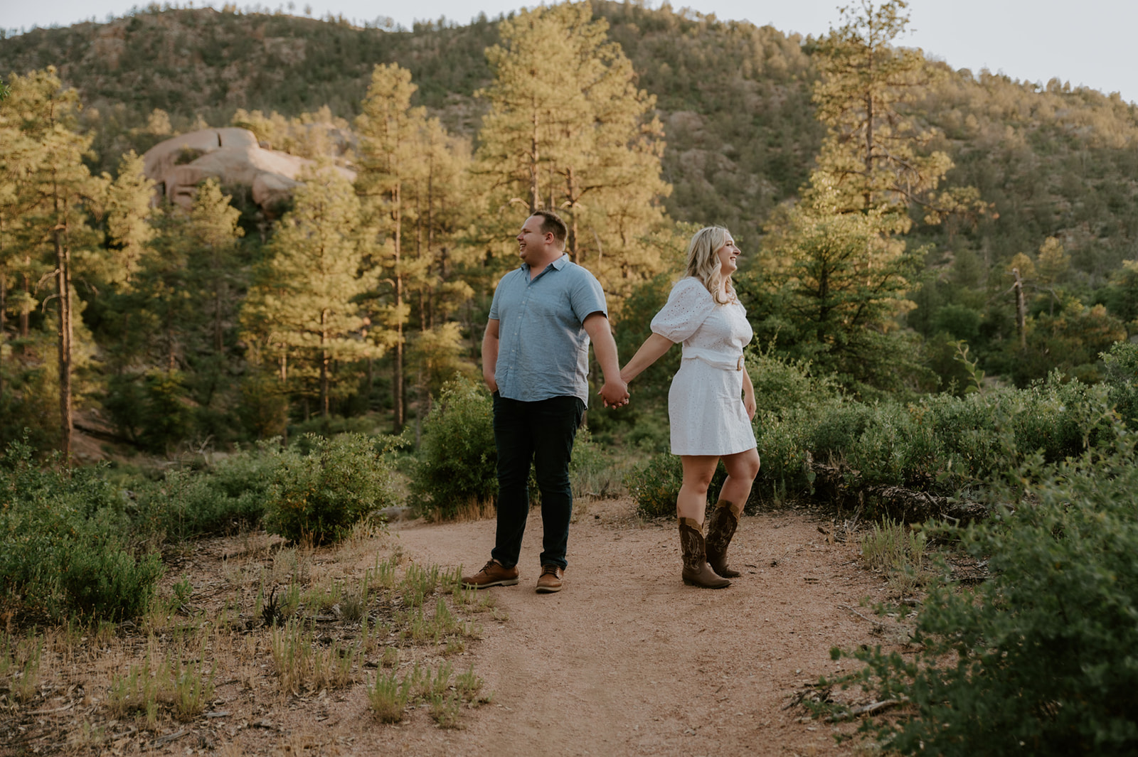 Couple holding hands and laughing while standing on a scenic forest path, a fun moment from an adventure elopement session
