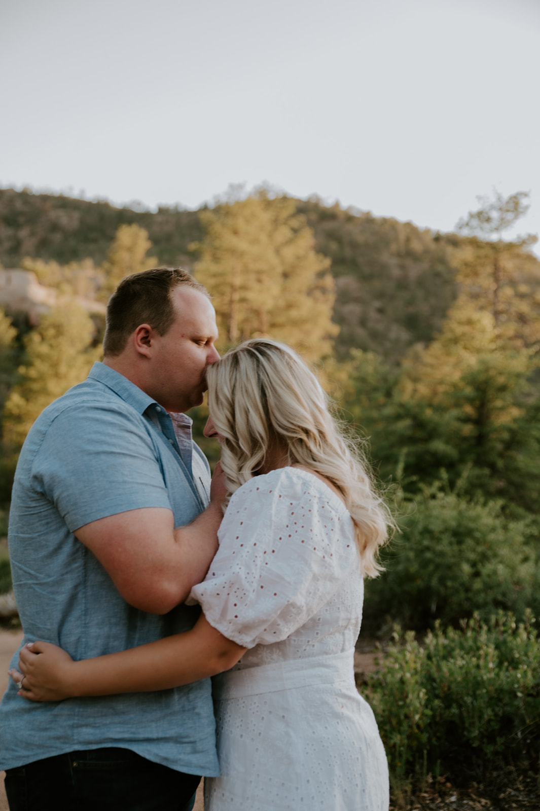 Couple sharing a quiet forehead kiss on a forest trail in Flagstaff during golden hour
