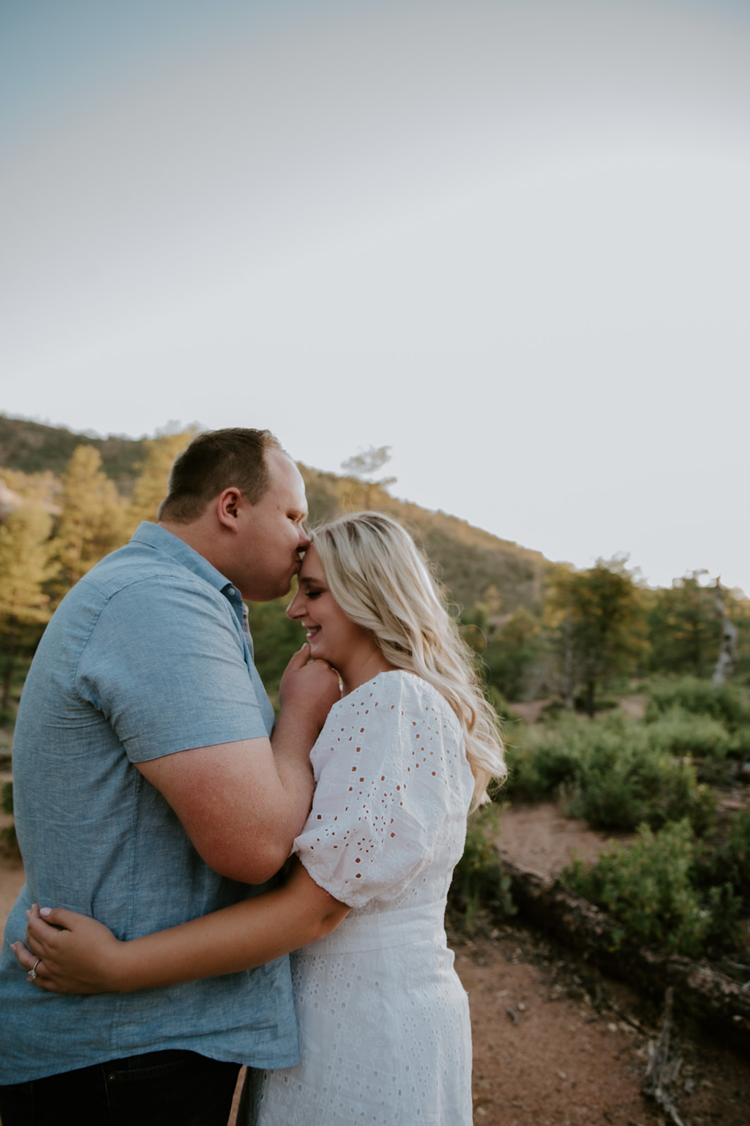 Couple sharing a quiet forehead kiss on a forest trail in Flagstaff during golden hour
