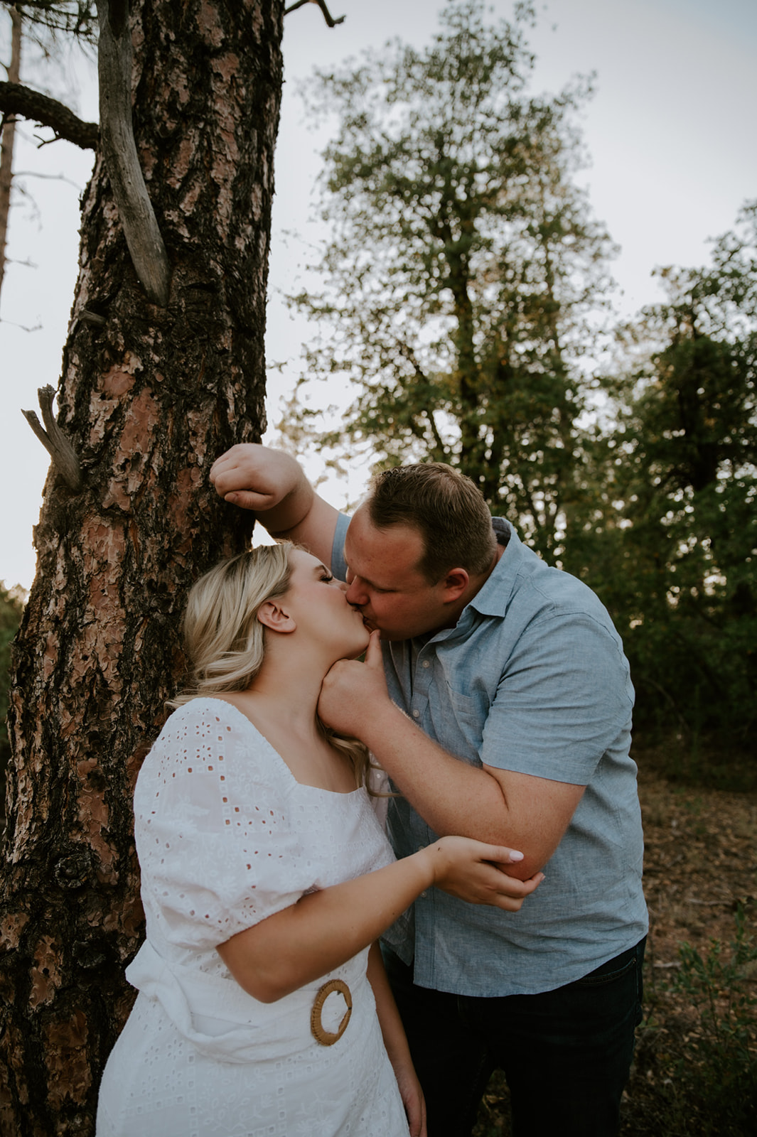 Couple kissing beside a tree in a forest setting, a candid moment from an adventure elopement session
