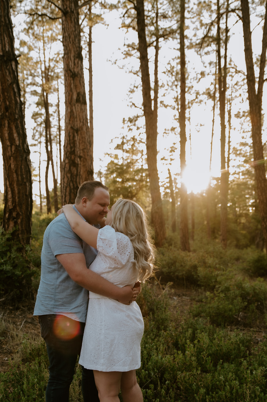 Couple embracing in a pine forest with golden sunlight filtering through the trees during an adventure elopement
