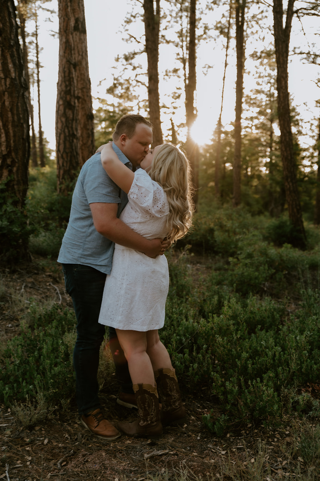Intimate forest moment as a couple embraces with sunlight glowing behind them
