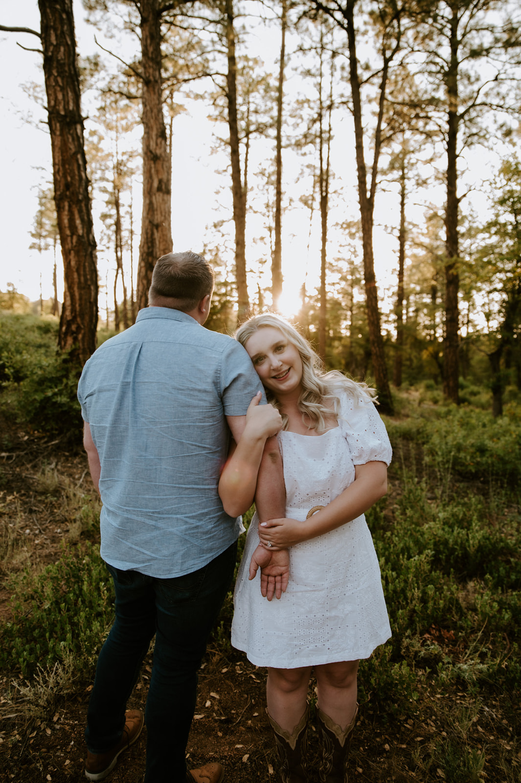 Bride smiling at the camera while holding her partner’s arm in a sunlit pine forest, perfect for adventure elopements

