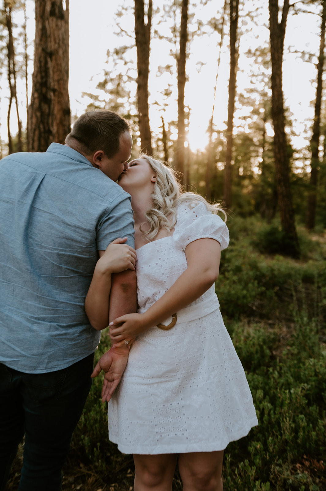 Playful kiss between a couple in the forest with golden sunlight filtering through tall pines, capturing the spirit of adventure elopements
