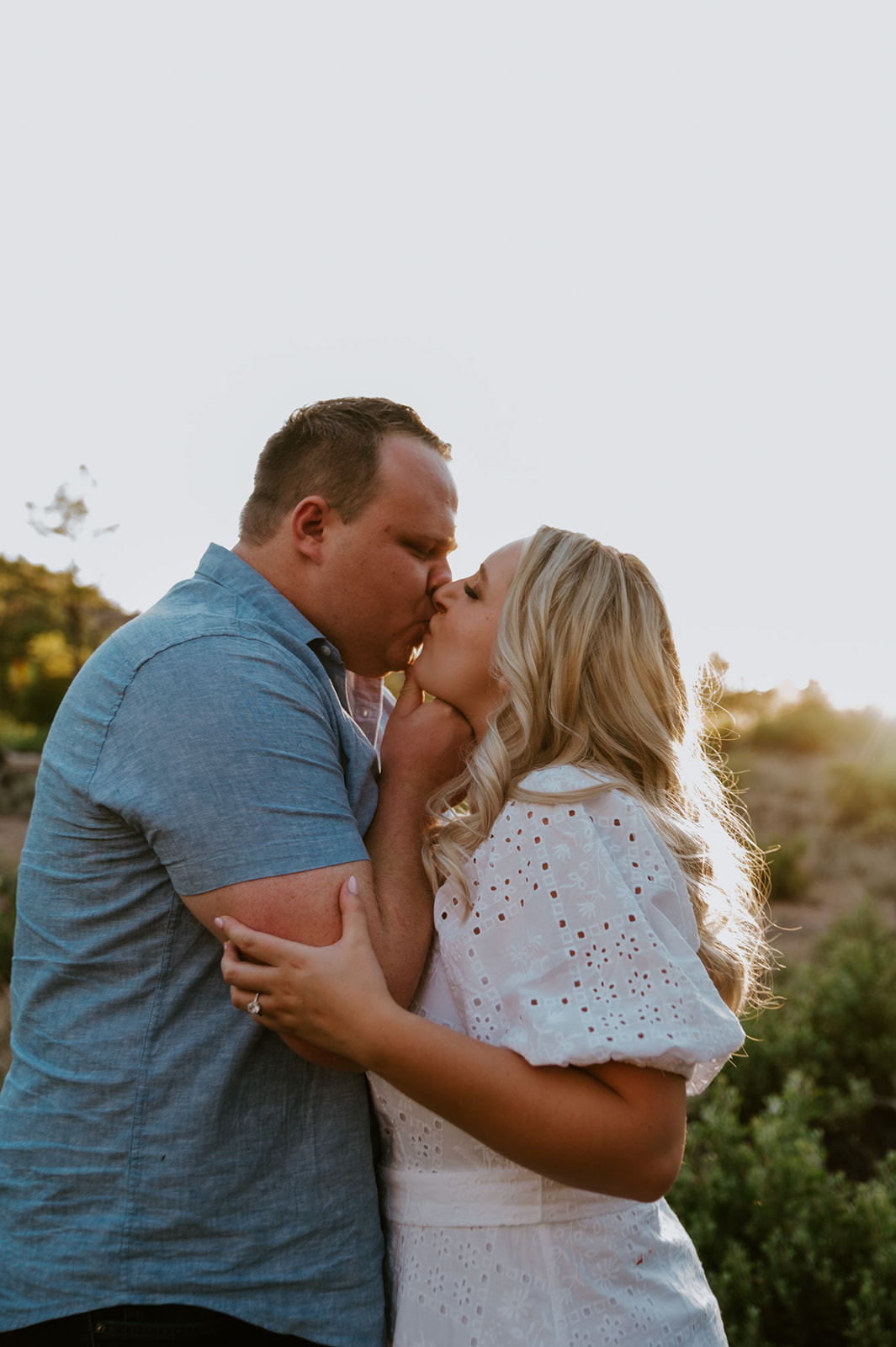 Close-up of a couple kissing with warm sunset light glowing through the trees behind them
