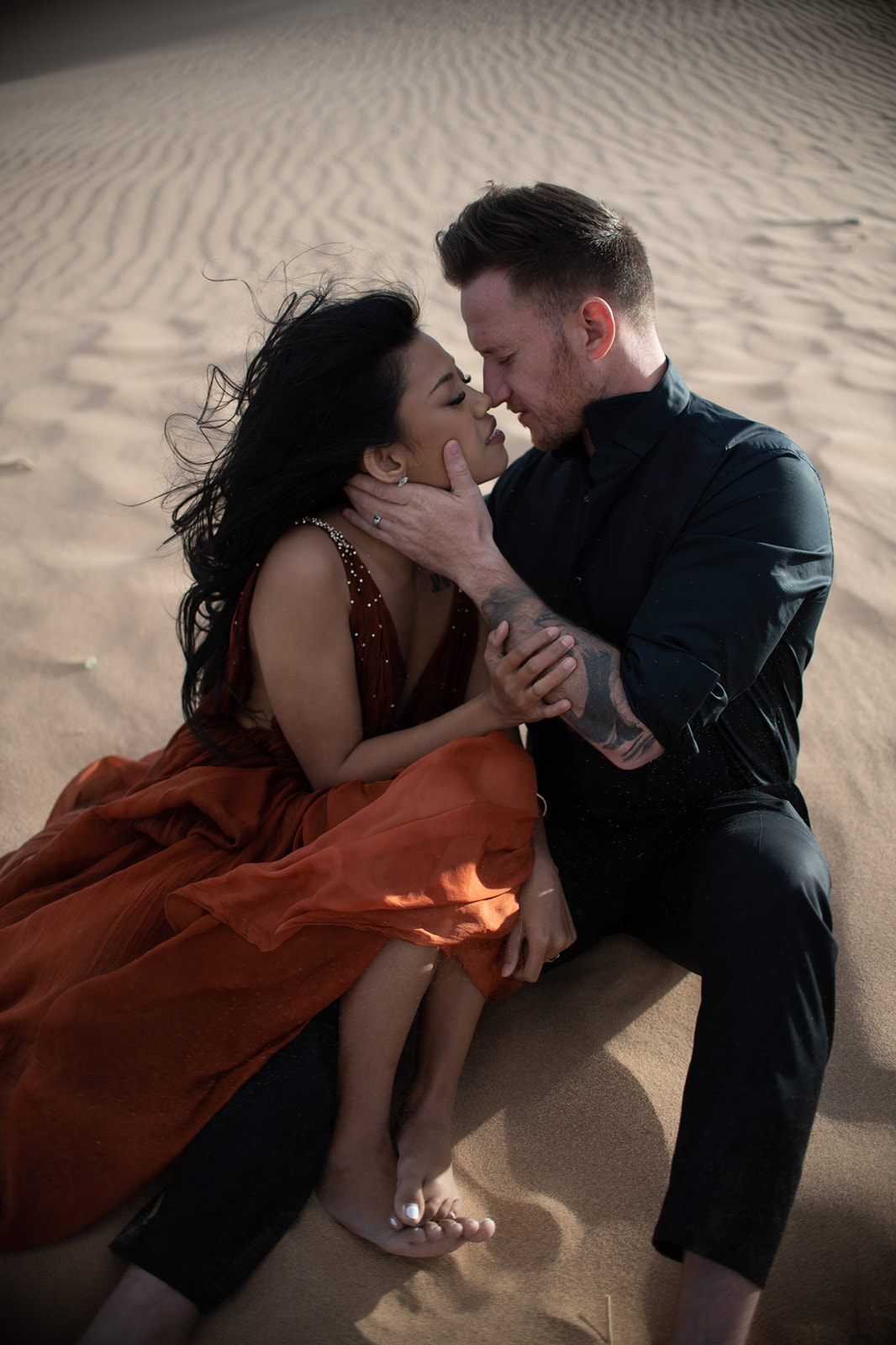 Close-up of couple sitting together in the sand, sharing an intimate moment with soft desert textures