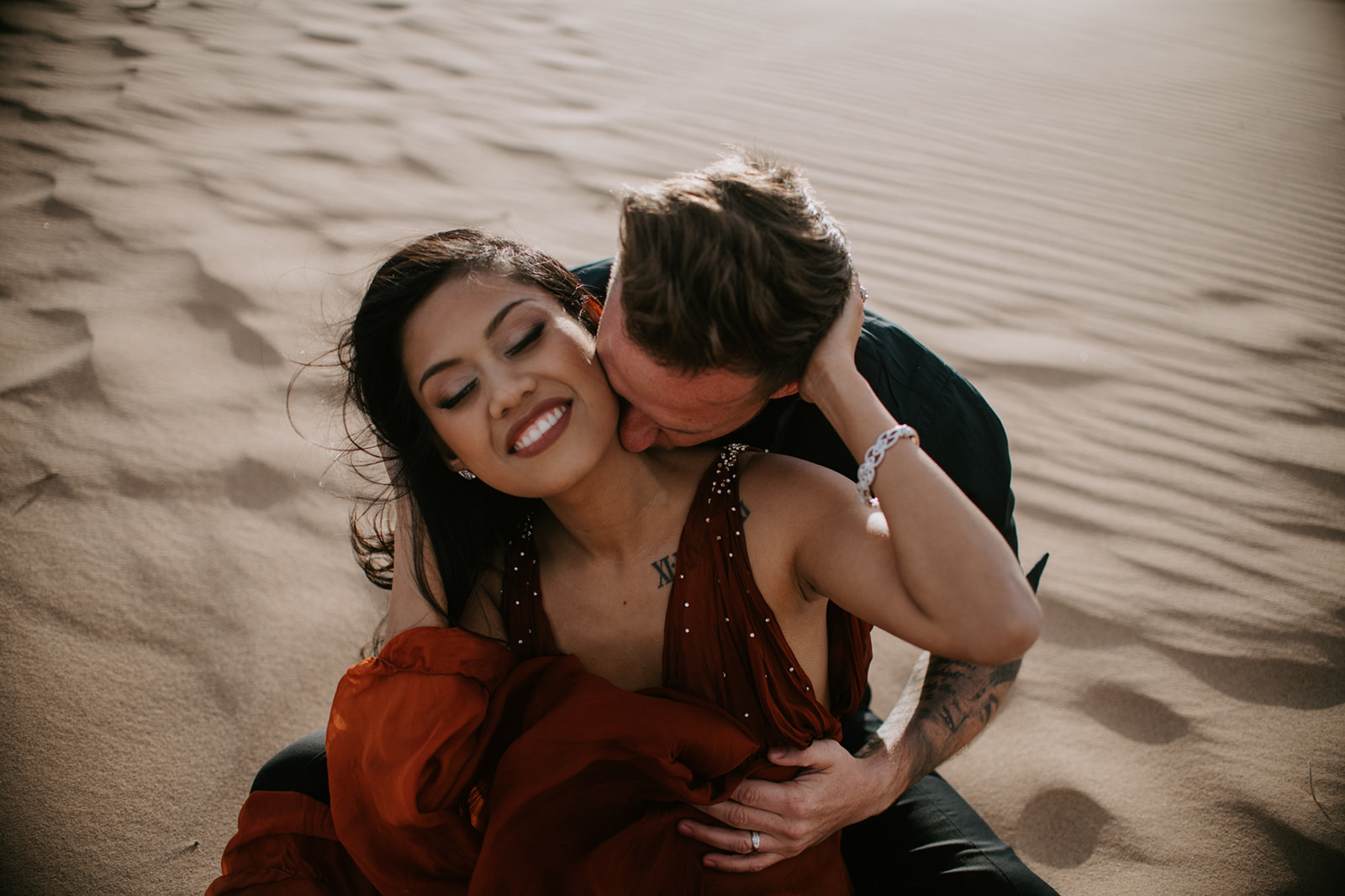 Playful candid moment of couple sitting in the sand, laughing and connecting during a desert engagement session
