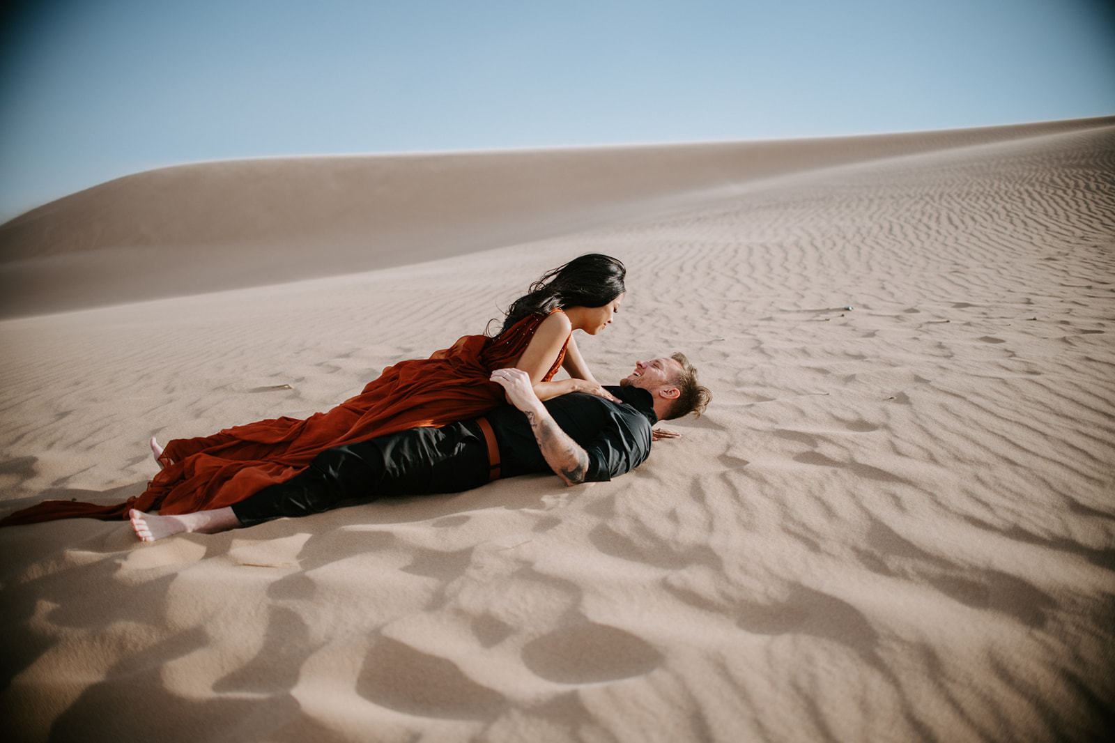 Couple laying together on rippled sand dunes, intimate and relaxed moment during a sand dunes photoshoot
