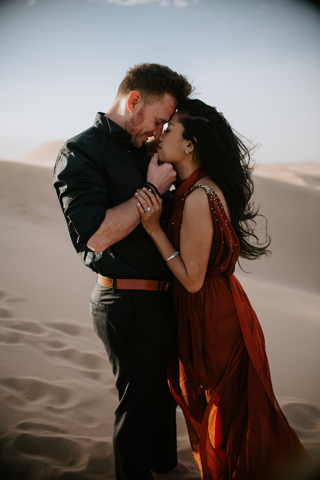 Close-up of couple leaning into each other on the dunes, soft light and wind adding movement and emotion
