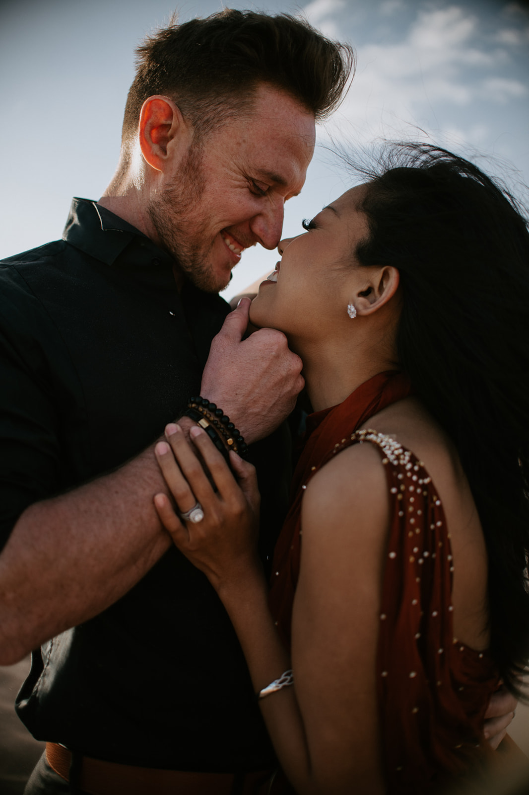 Close-up of couple smiling and leaning into each other, soft wind and intimate desert connection
