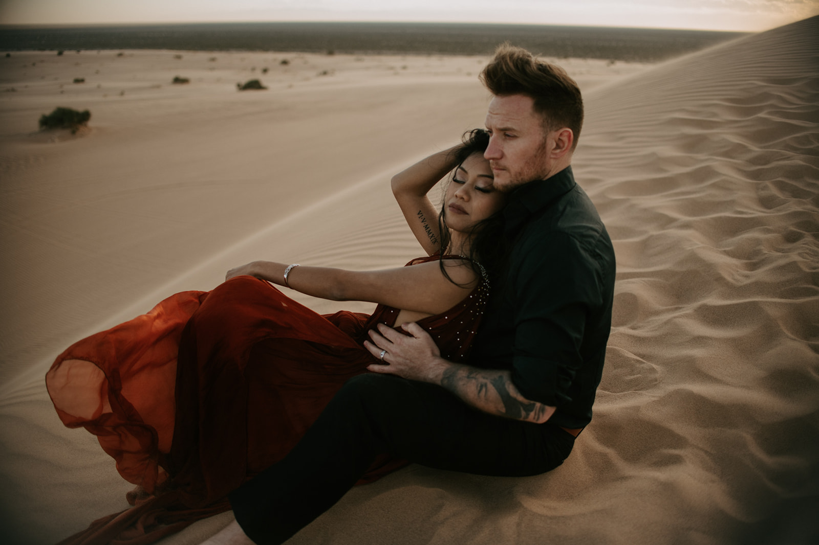 Couple sitting together on rippled sand dunes, relaxed and intimate moment with warm desert tones
