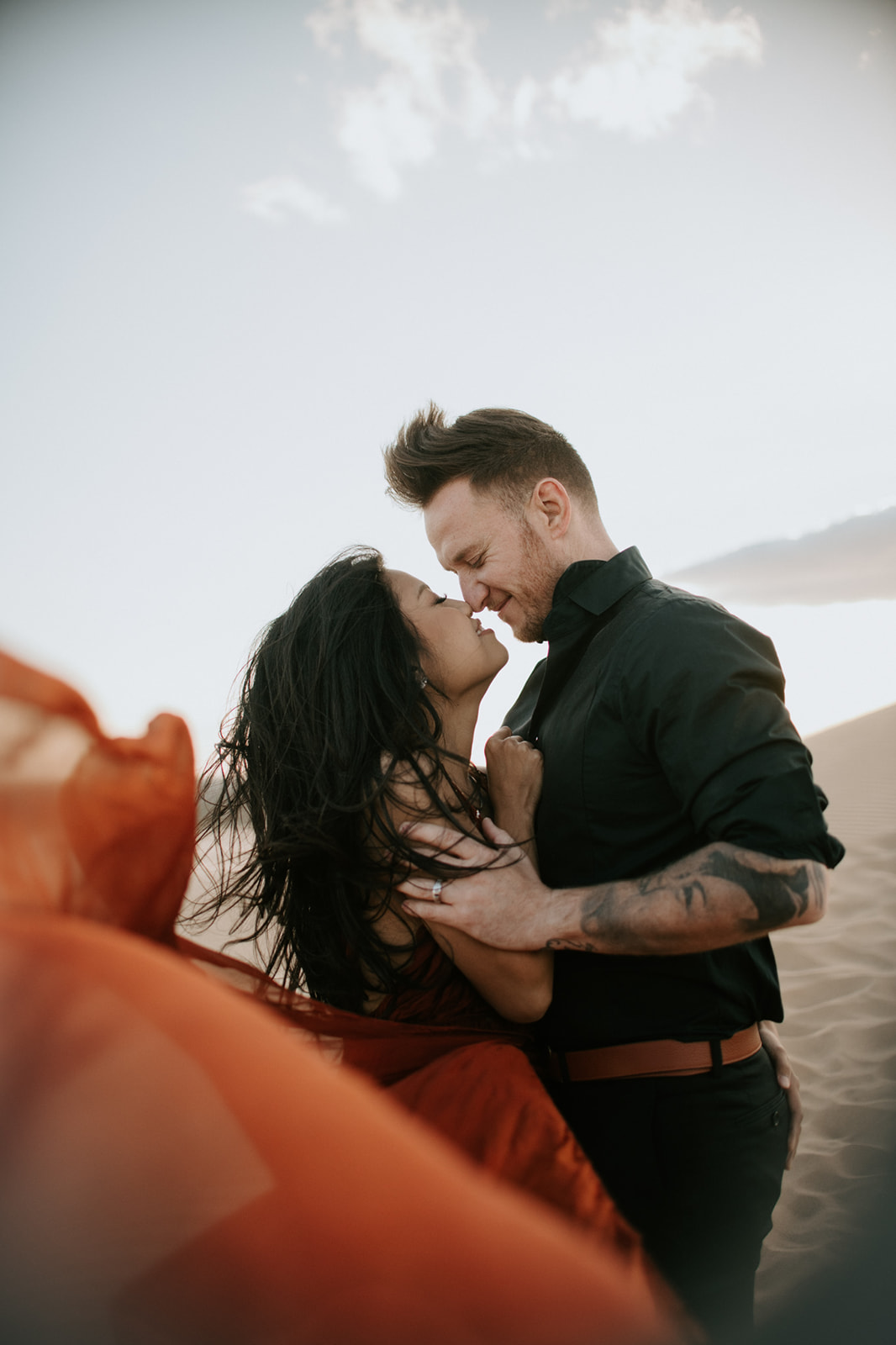Couple embracing on the sand dunes with flowing red dress and soft light during a sand dunes photoshoot

