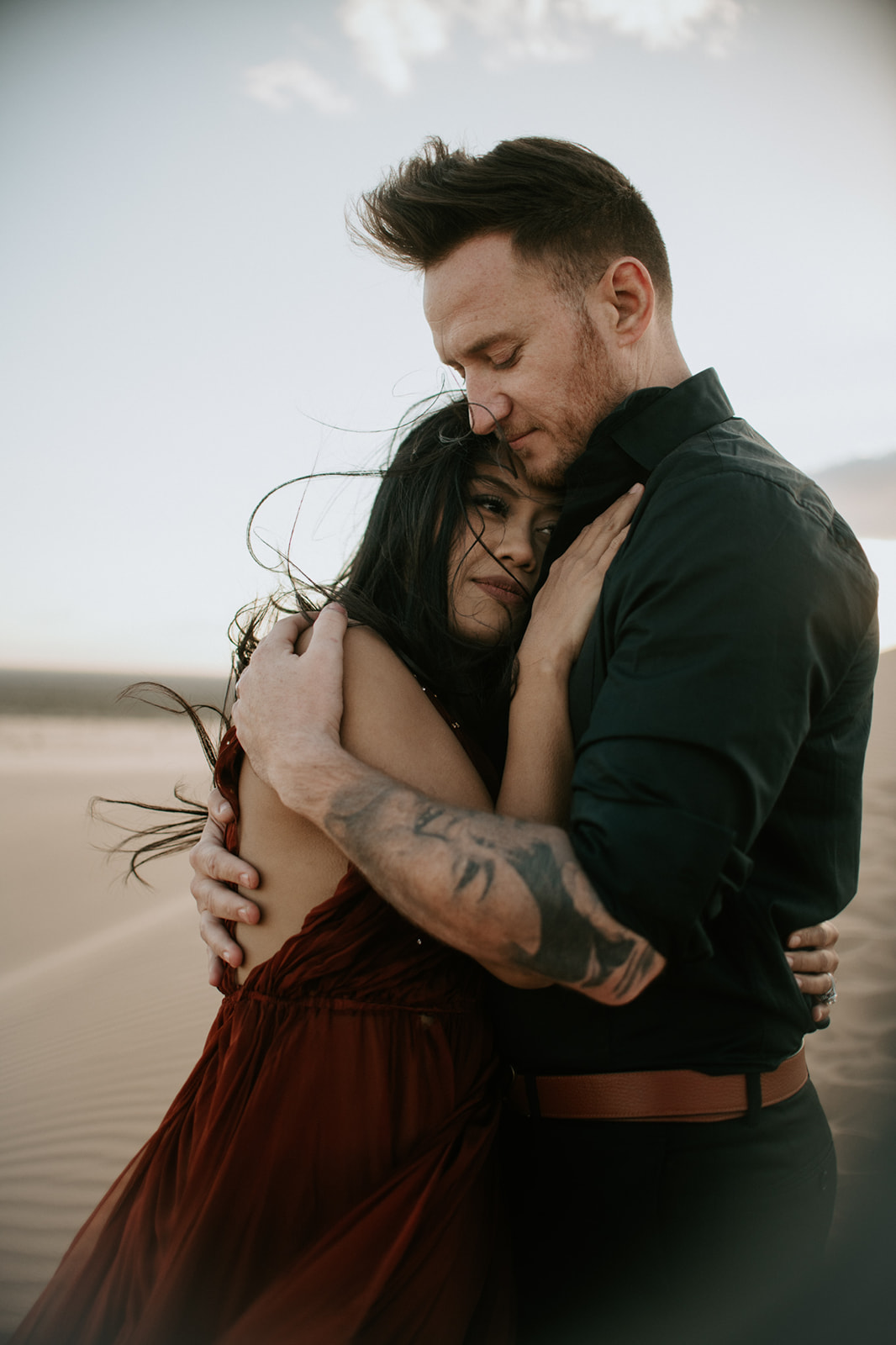 Close-up of couple embracing on the dunes, wind moving through her hair during an intimate sand dunes photoshoot
