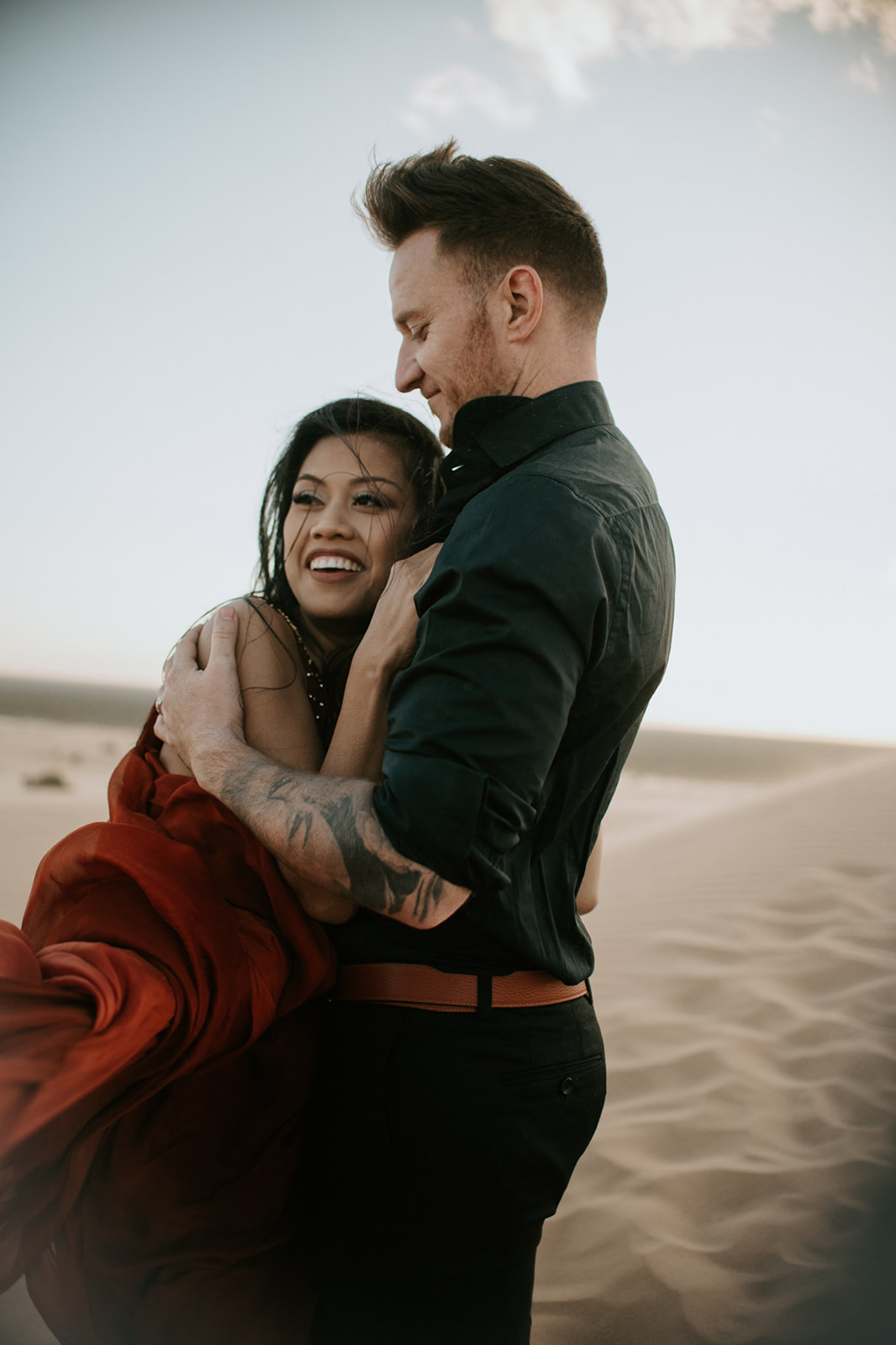 Close-up of couple leaning into each other on the dunes, soft light and wind creating an intimate desert moment