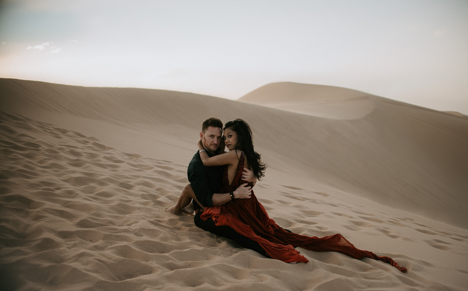 Couple sitting together in soft sand dunes, relaxed and intimate moment with neutral desert tones
