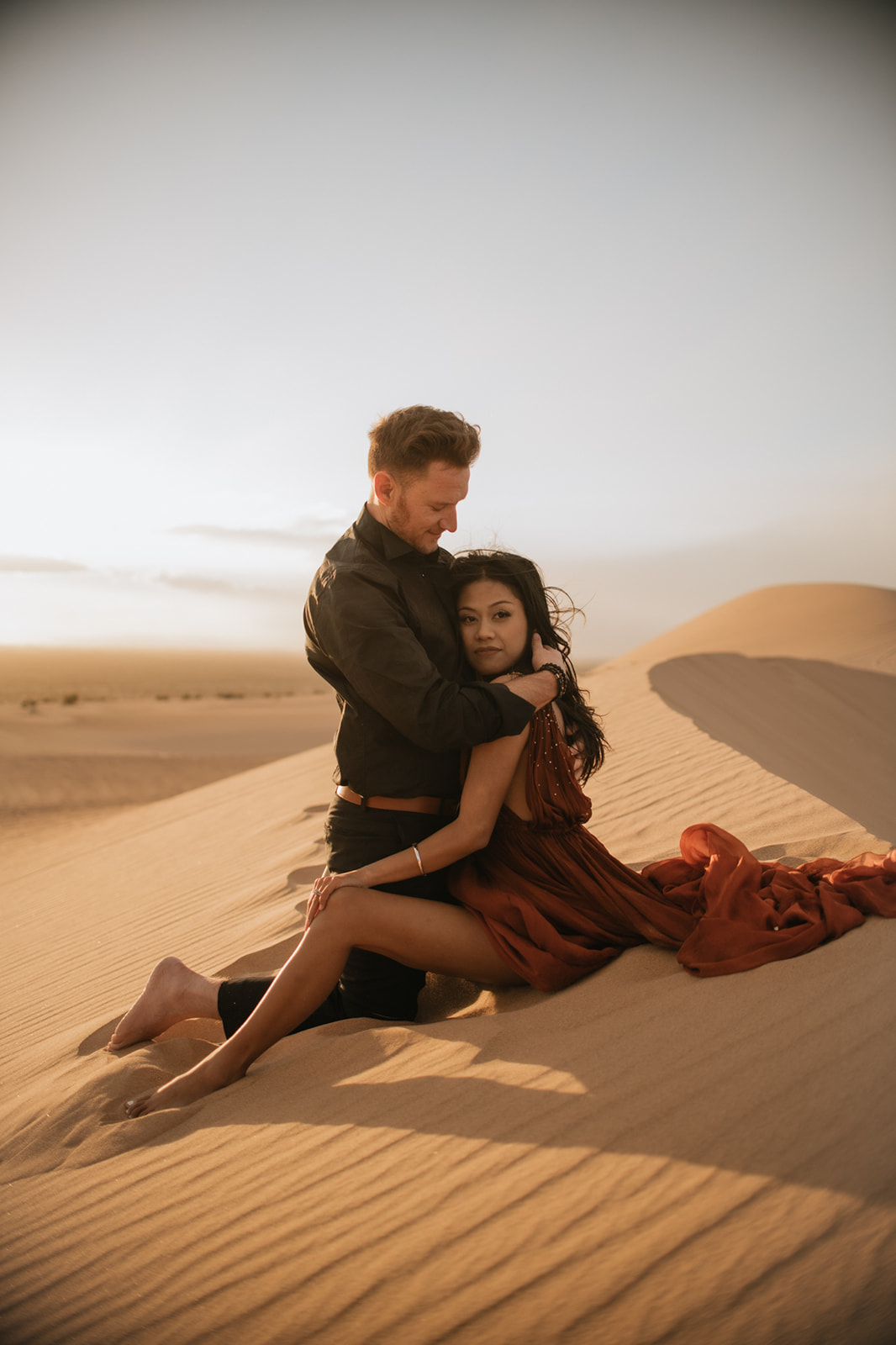 Couple embracing on a dune at sunset, golden light wrapping around them during a sand dunes photoshoot
