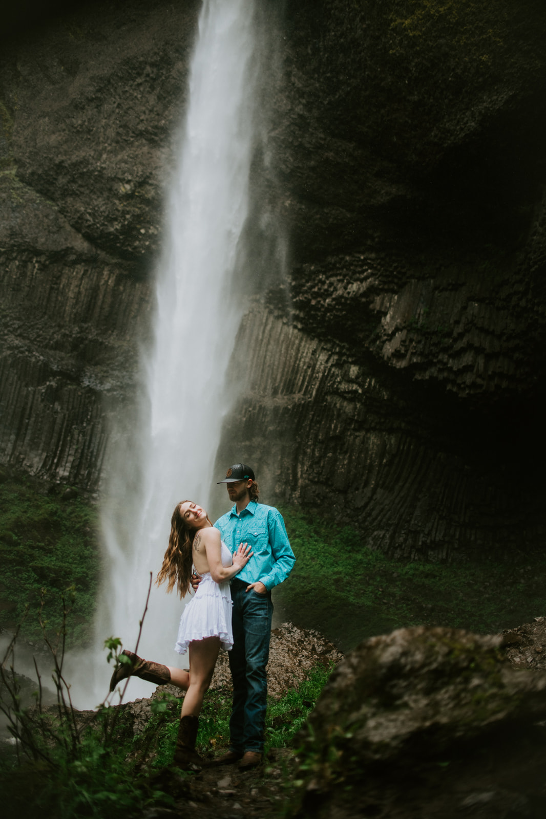 Couple standing in front of Latourell Falls with dramatic cliffs and flowing water, Oregon engagement session