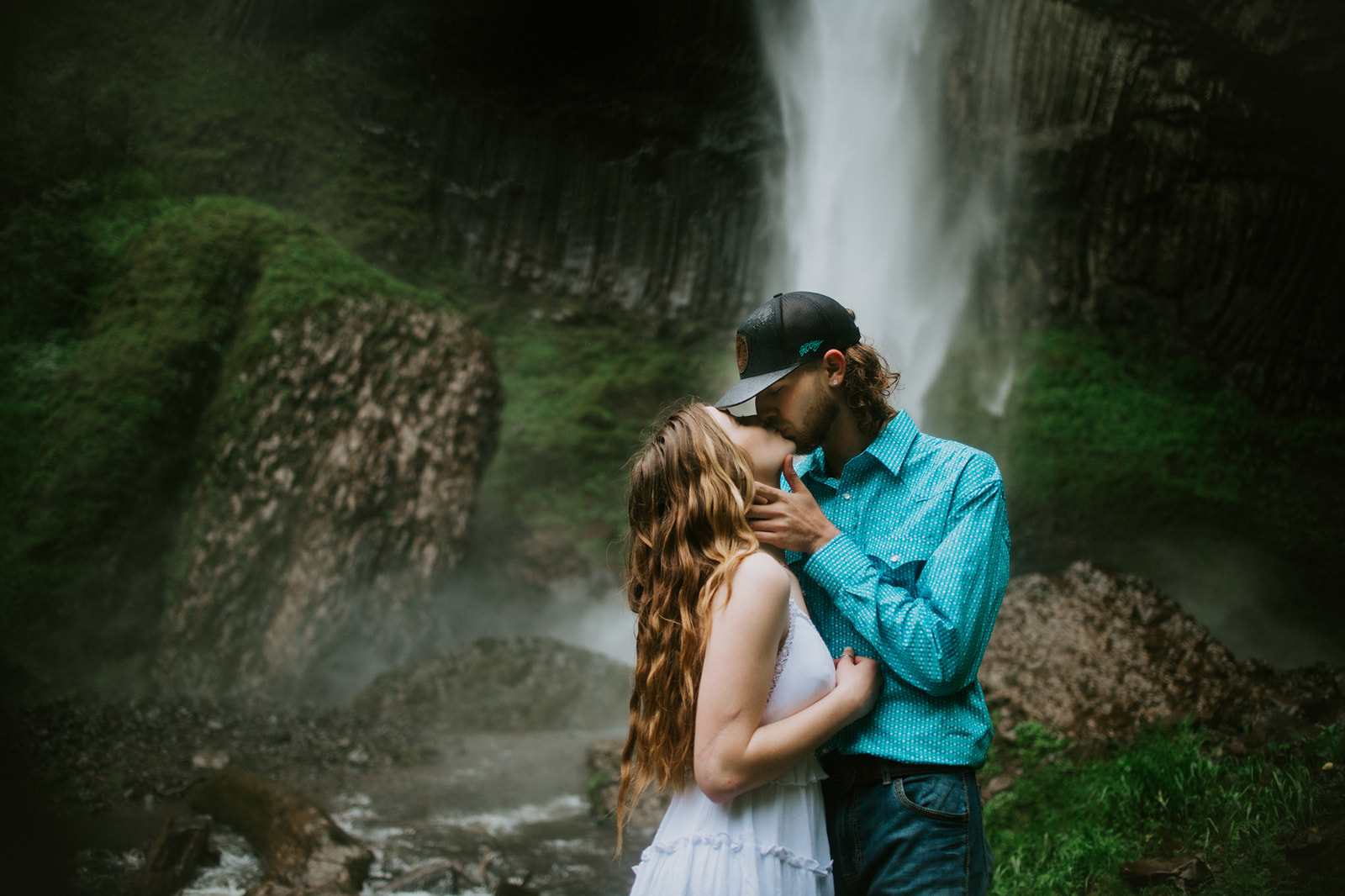 Couple kissing in front of Latourell Falls with mist and cliffs surrounding them during outdoor engagement photos