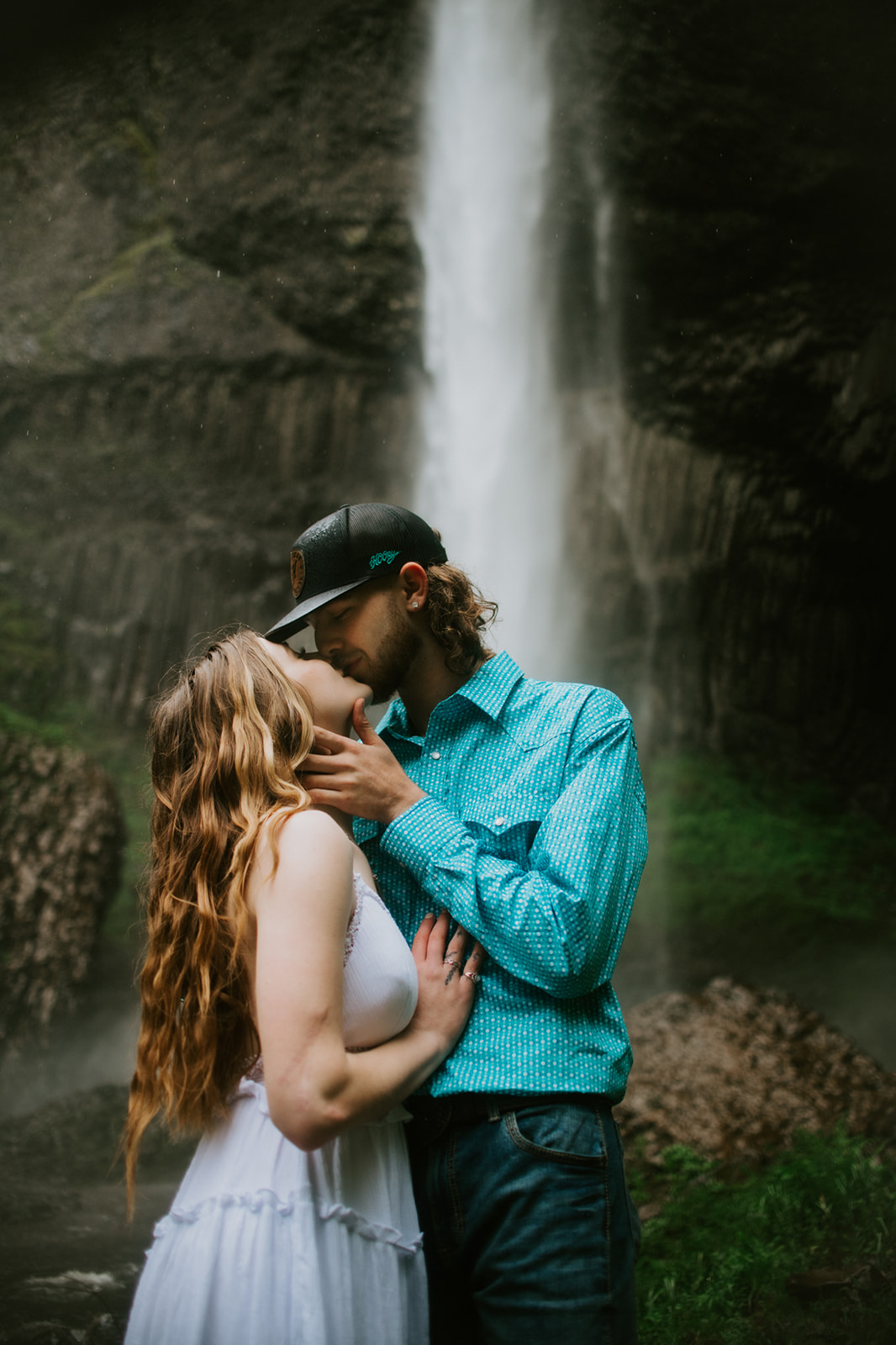 Close-up of couple kissing with waterfall behind them, soft mist and natural movement captured