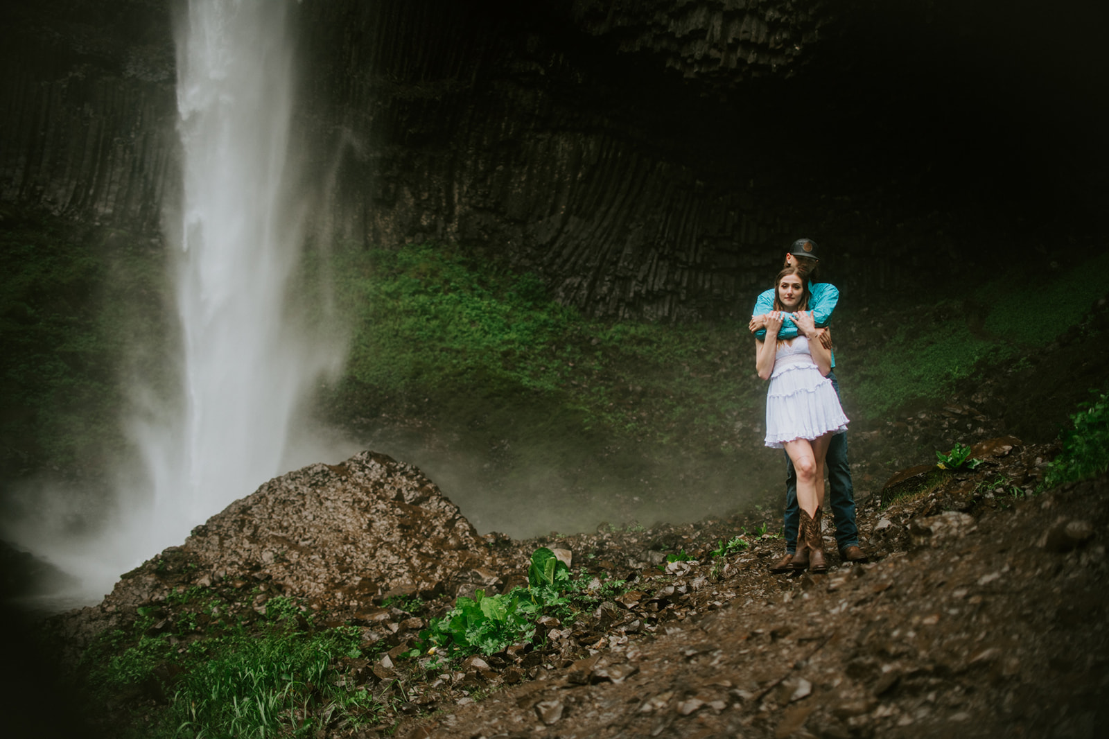 Couple embracing from behind near waterfall with mist and textured rock wall backdrop