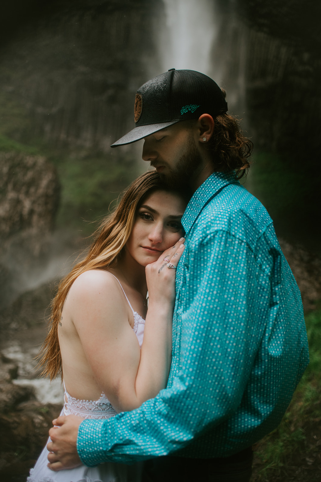 Couple hugging closely with waterfall behind them, emotional and intimate engagement moment