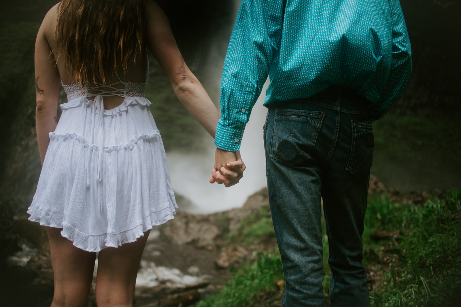 Close-up of couple holding hands with waterfall in the background, intimate outdoor engagement photos