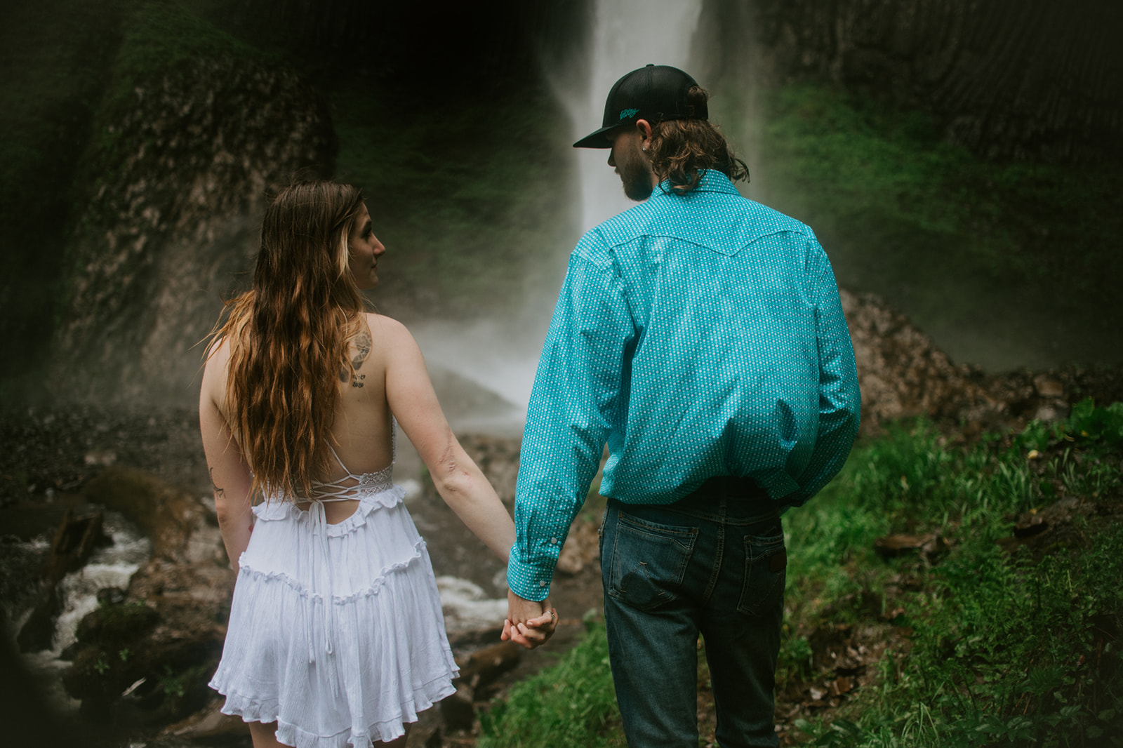Couple walking hand in hand toward waterfall, quiet and connected outdoor engagement photos