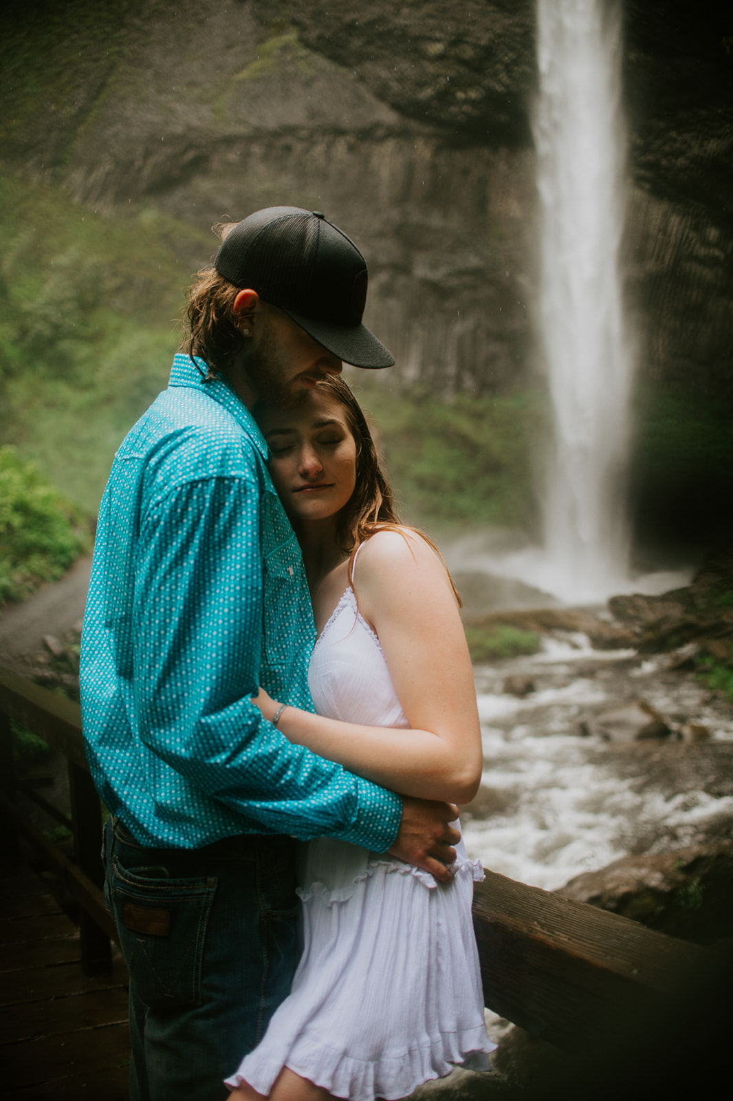 Couple standing together near waterfall with dramatic cliffs and soft mist surrounding them