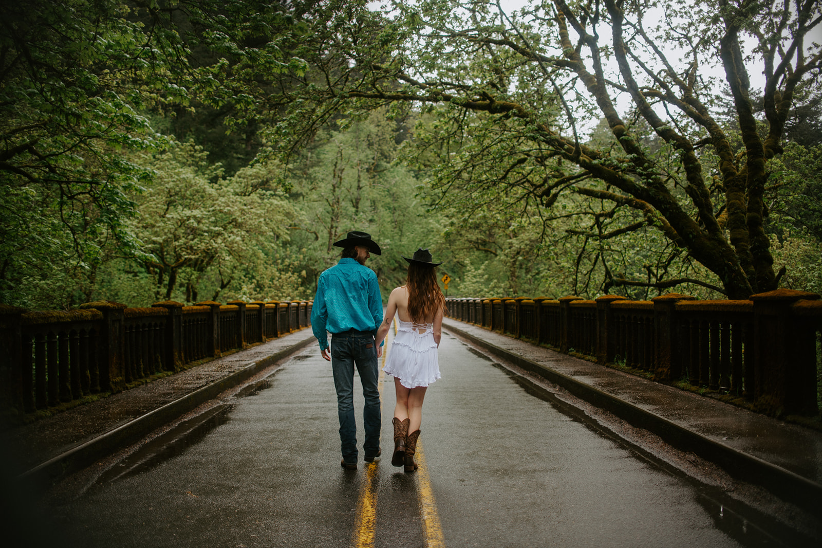 Couple walking down wet forest road hand in hand, cinematic outdoor engagement photos