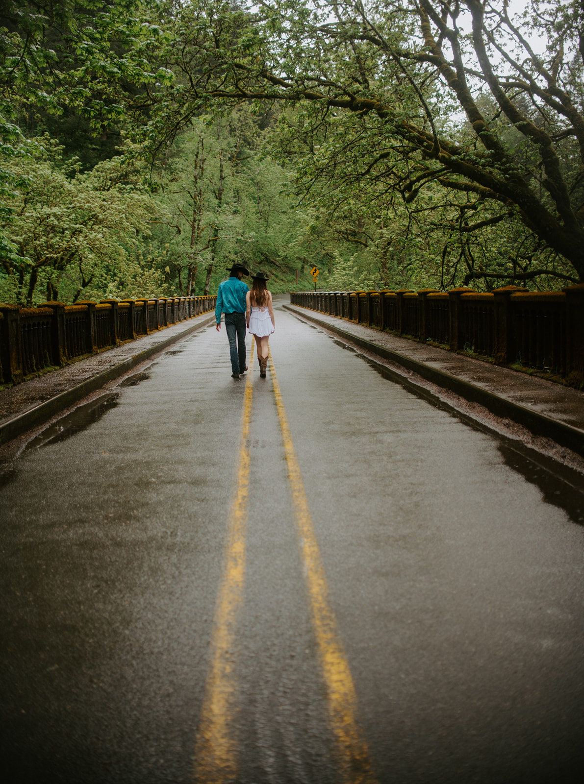 Couple walking down a quiet forest road holding hands, relaxed and candid outdoor engagement photos