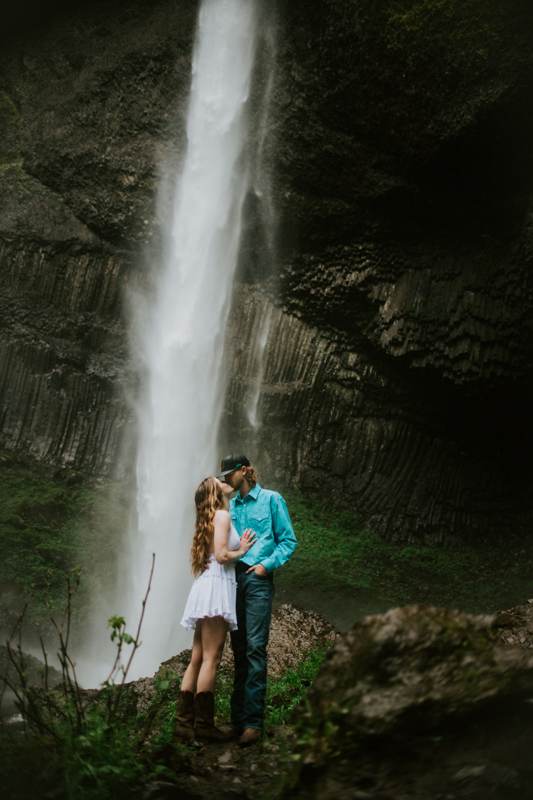 Adventurous engagement photoshoot with couple kissing in front of a dramatic waterfall surrounded by lush greenery
