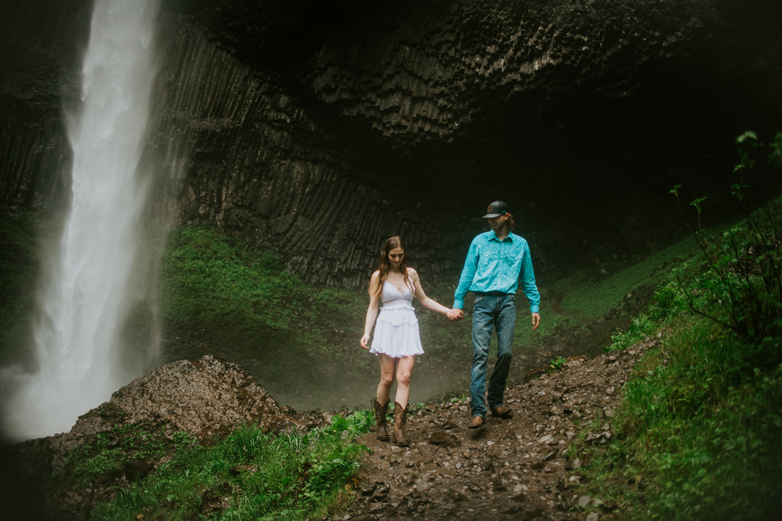 Close-up of couple kissing in front of a moody waterfall surrounded by dark rock and mist