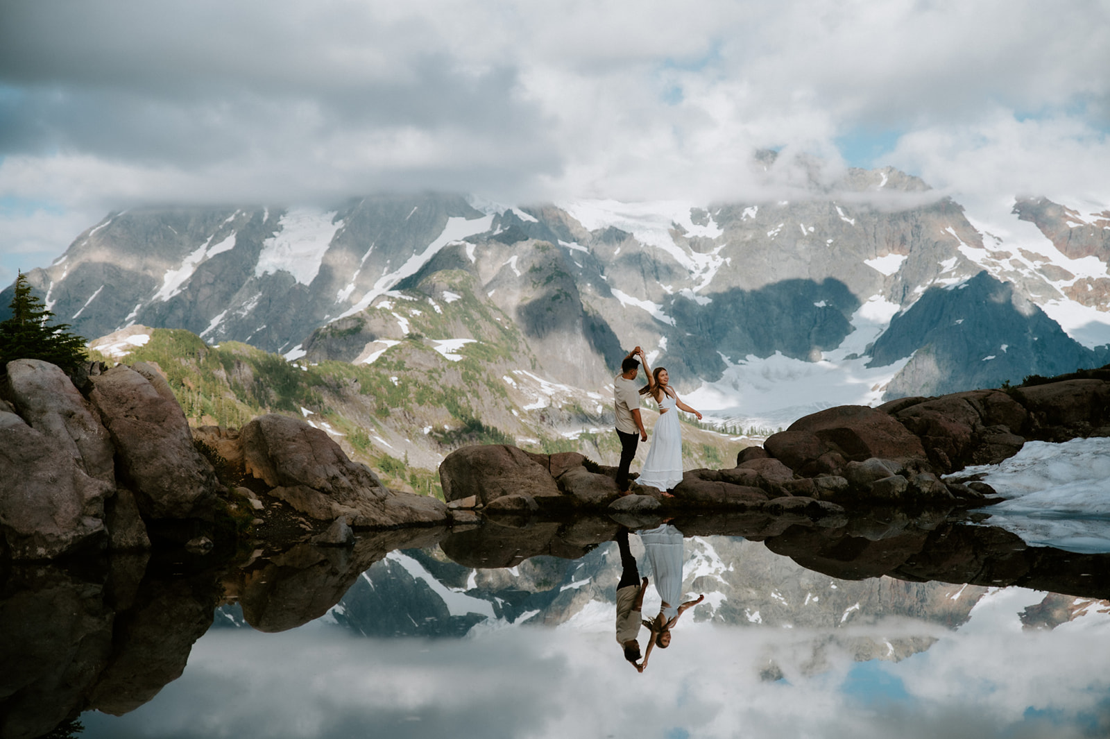 Epic engagement photoshoot with couple dancing on rocks reflected in a glassy alpine lake