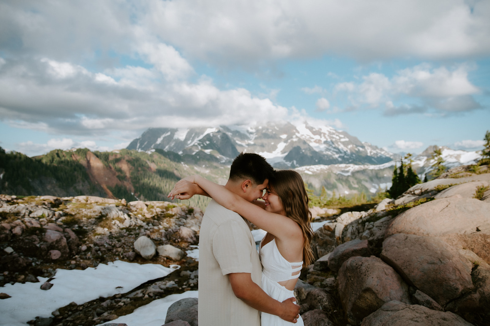 Scenic engagement photoshoot with couple embracing in the mountains with dramatic peaks and soft light behind them