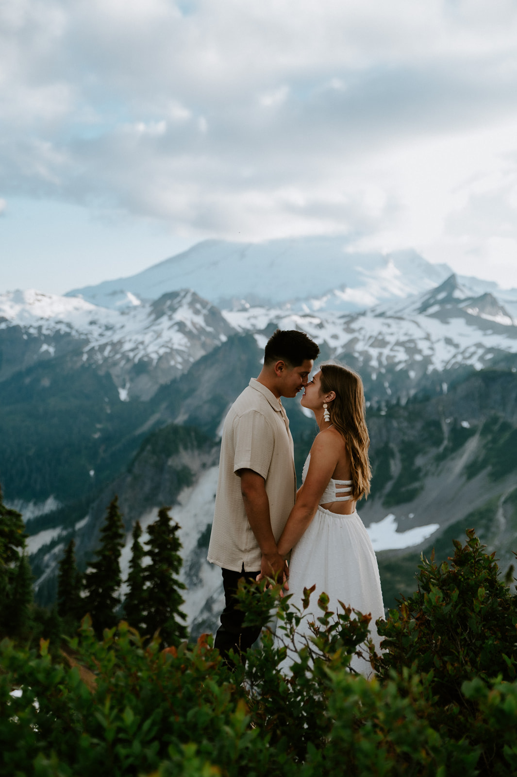 Intimate engagement photoshoot with couple holding hands in front of snowy mountain peaks and alpine views