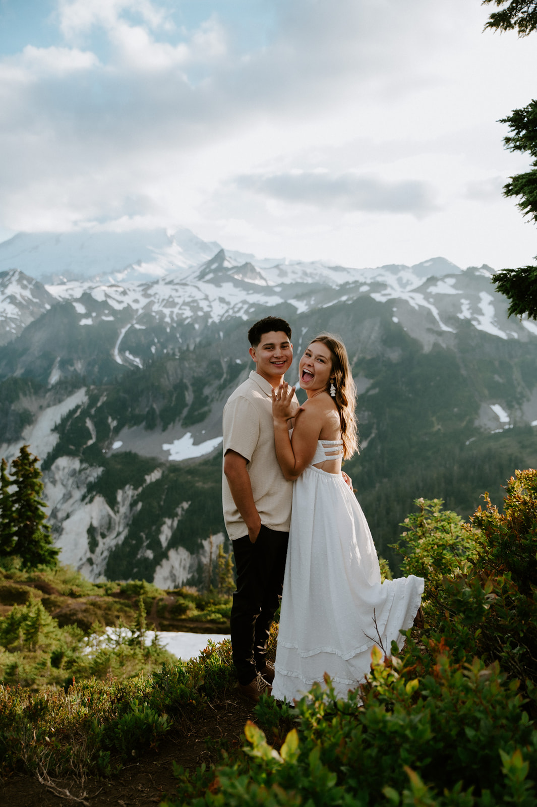 Playful engagement photoshoot with couple laughing together on a mountain overlook with sweeping alpine views