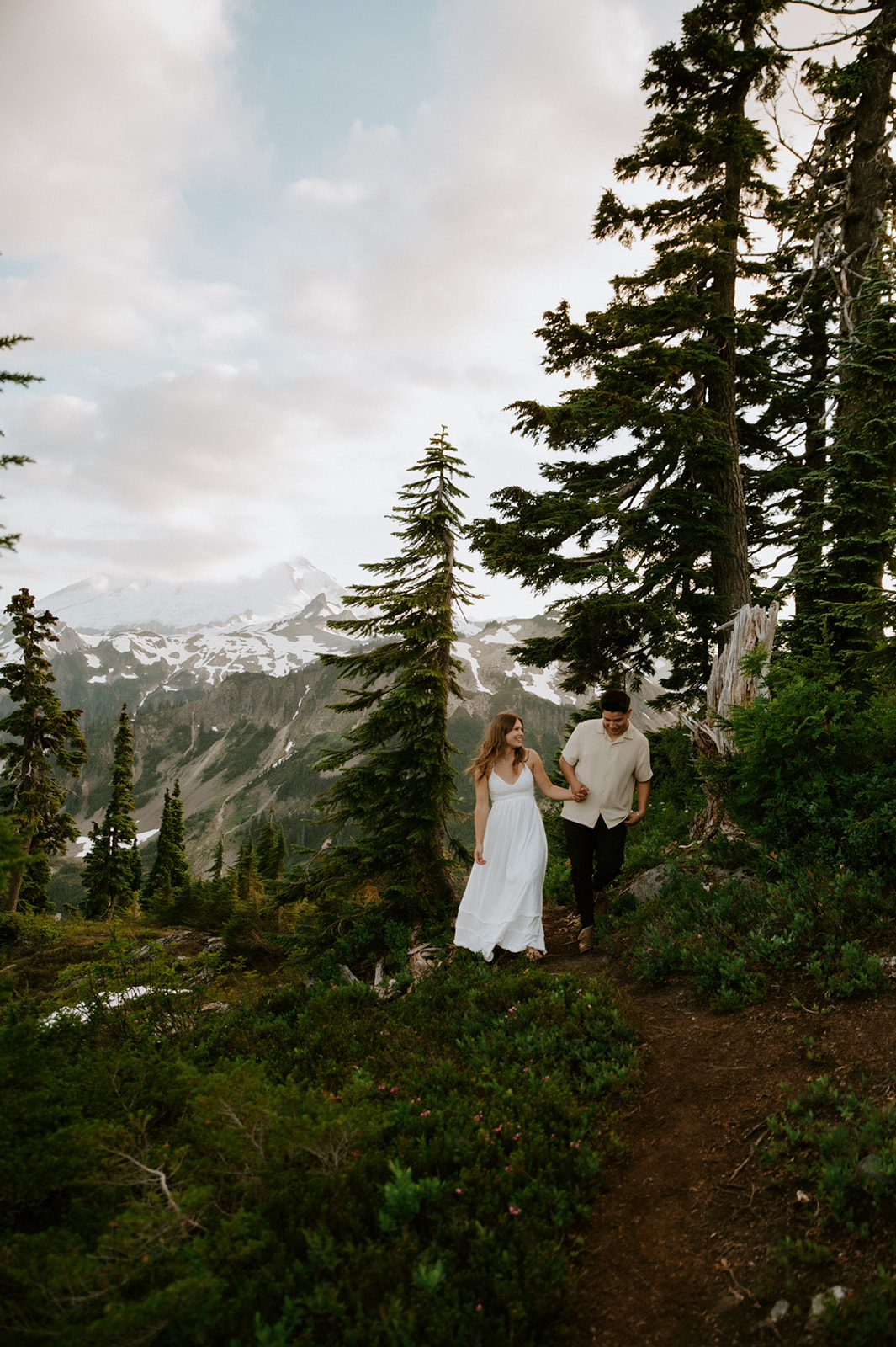 Couple walking hand in hand along a forested mountain trail with expansive alpine views