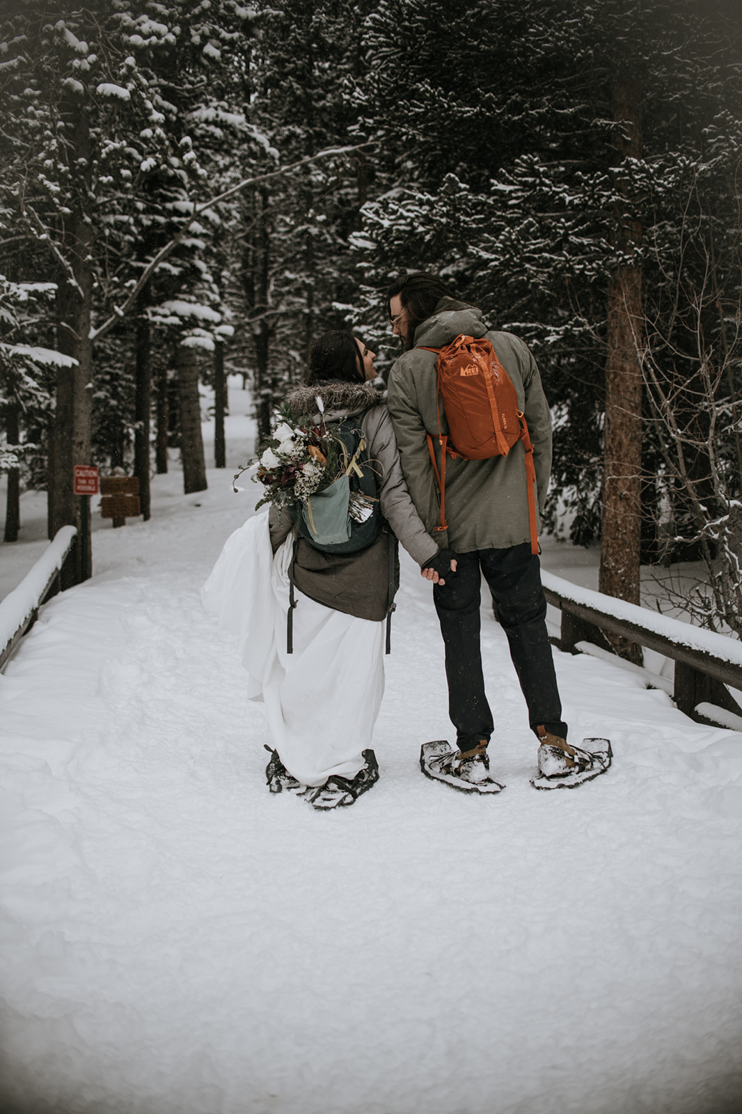 Couple hiking through a snowy forest in winter gear, holding hands on a quiet trail