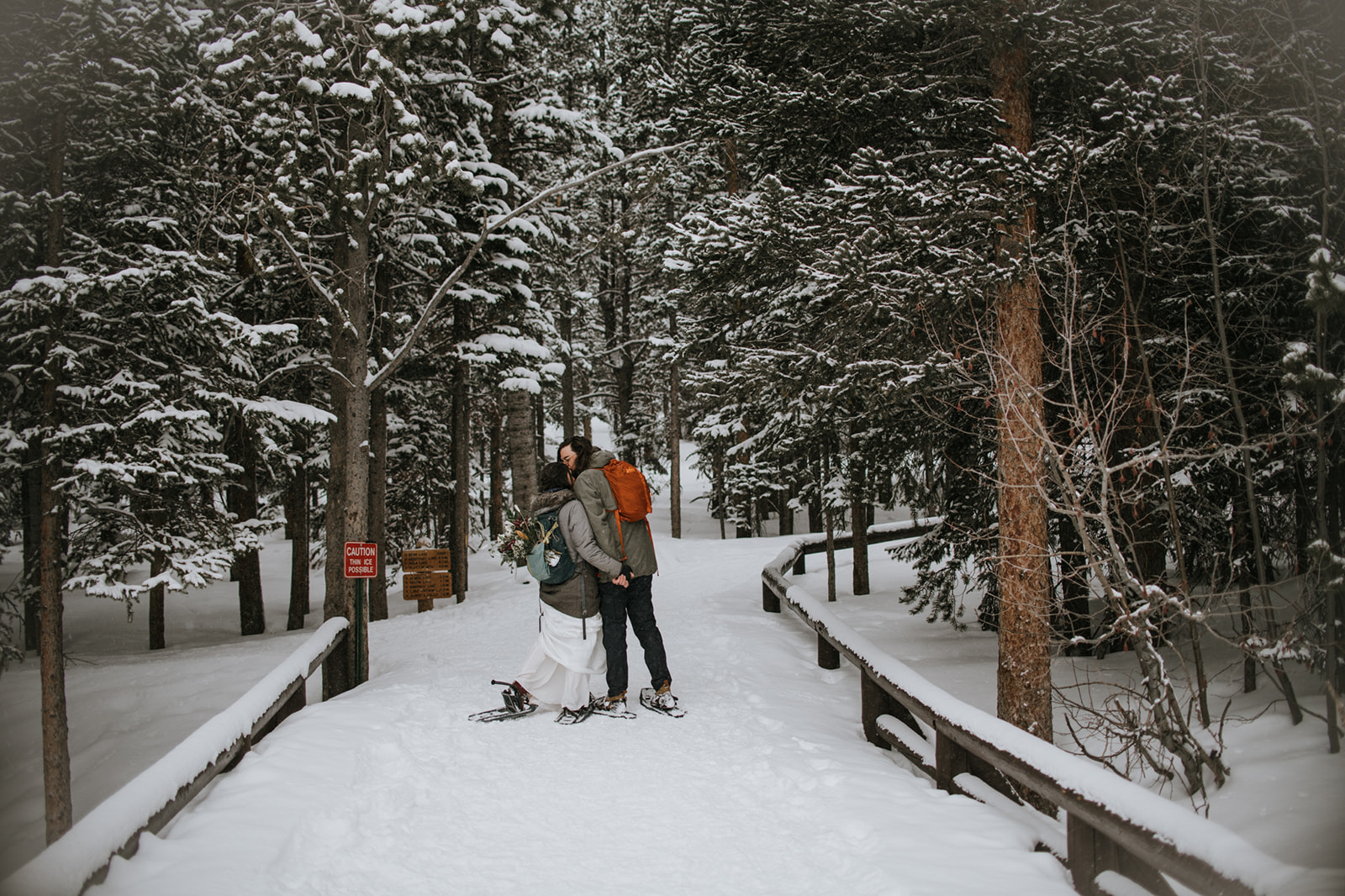 Adventurous winter engagement photoshoot with couple hiking through a snowy forest in snowshoes