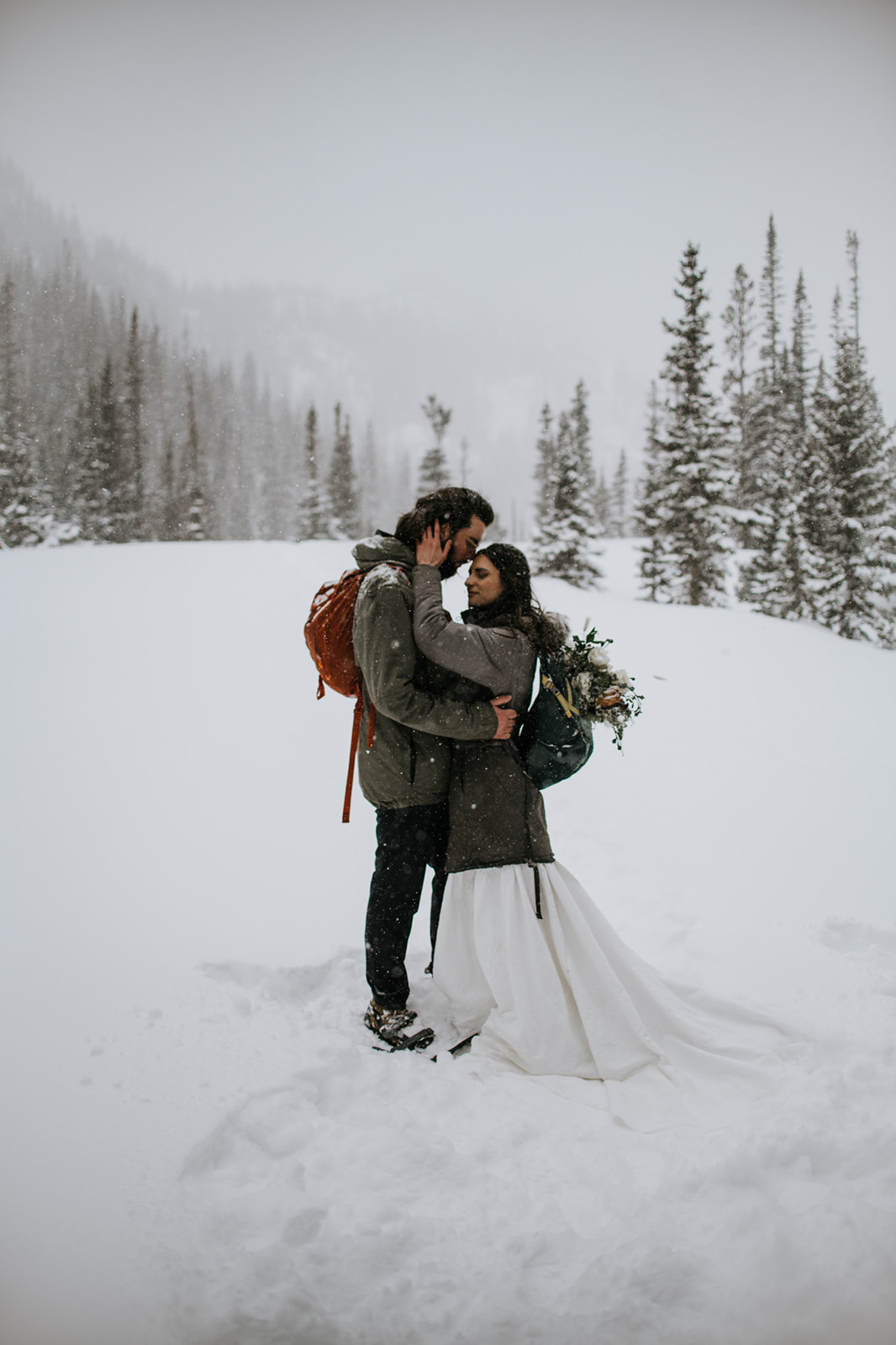Intimate winter engagement photoshoot with couple embracing in a snowy landscape with evergreen trees in the background