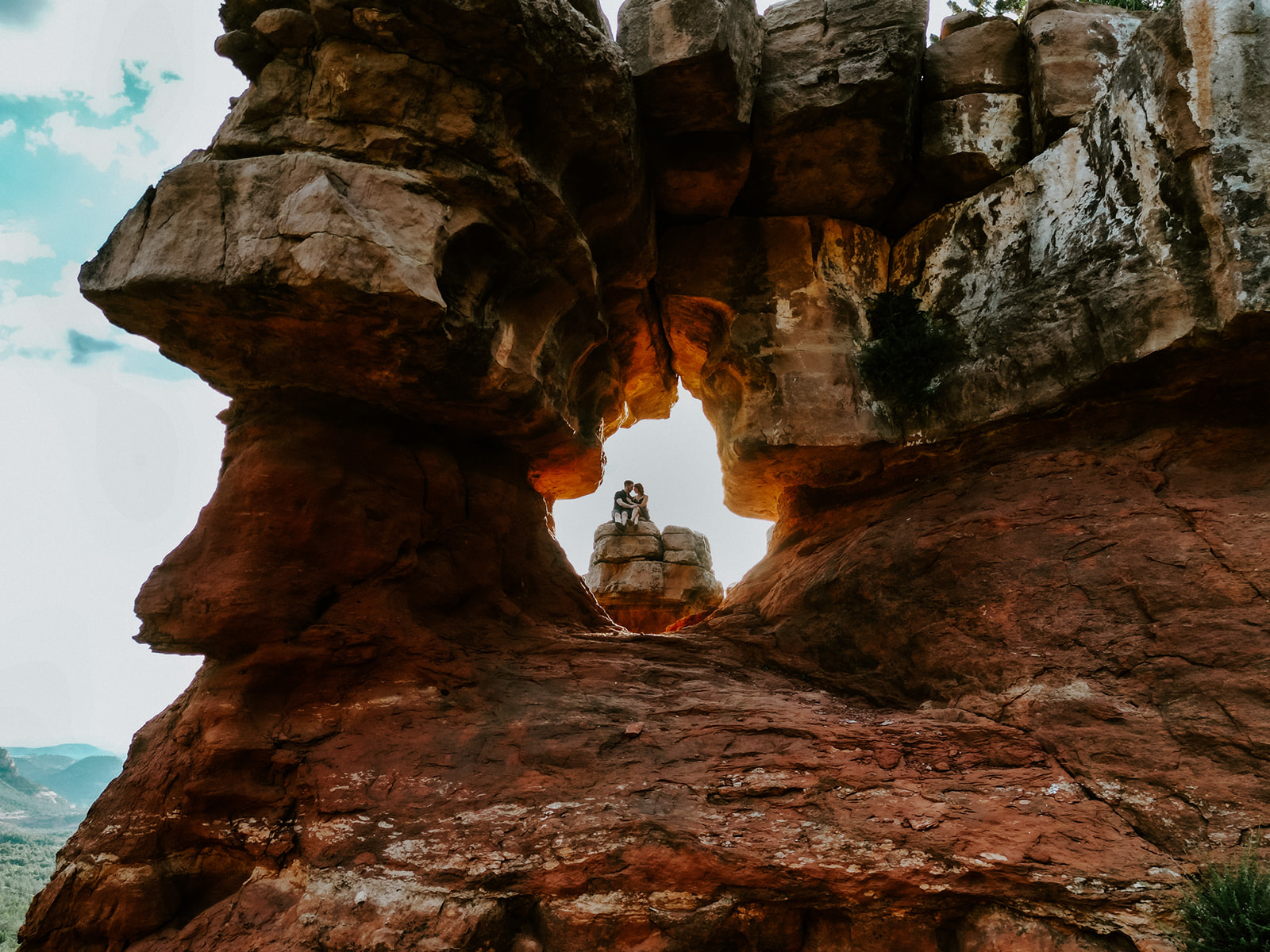 Wide shot of a couple sitting inside a natural rock arch formation during a Sedona adventure session
