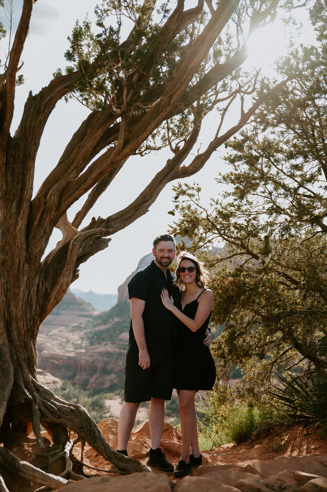 Couple standing under a twisted tree with sunlight filtering through during their Sedona engagement session