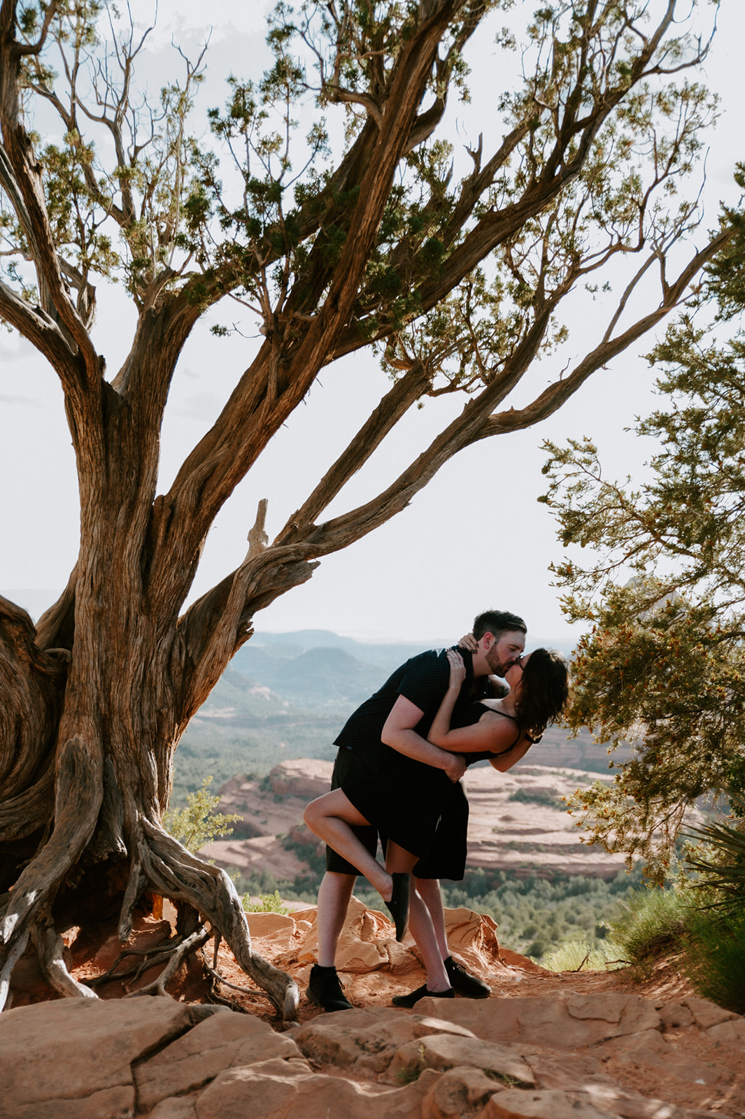 Couple kissing under a twisted tree with sweeping Sedona views in the background