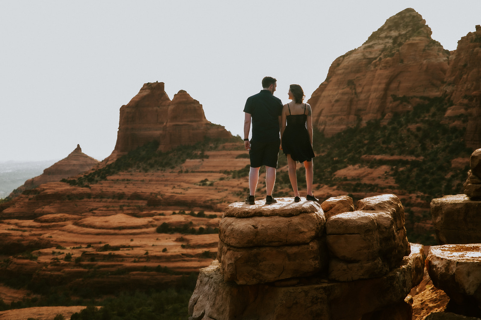 Couple standing on a rock ledge overlooking Sedona’s layered red rock landscape at sunset