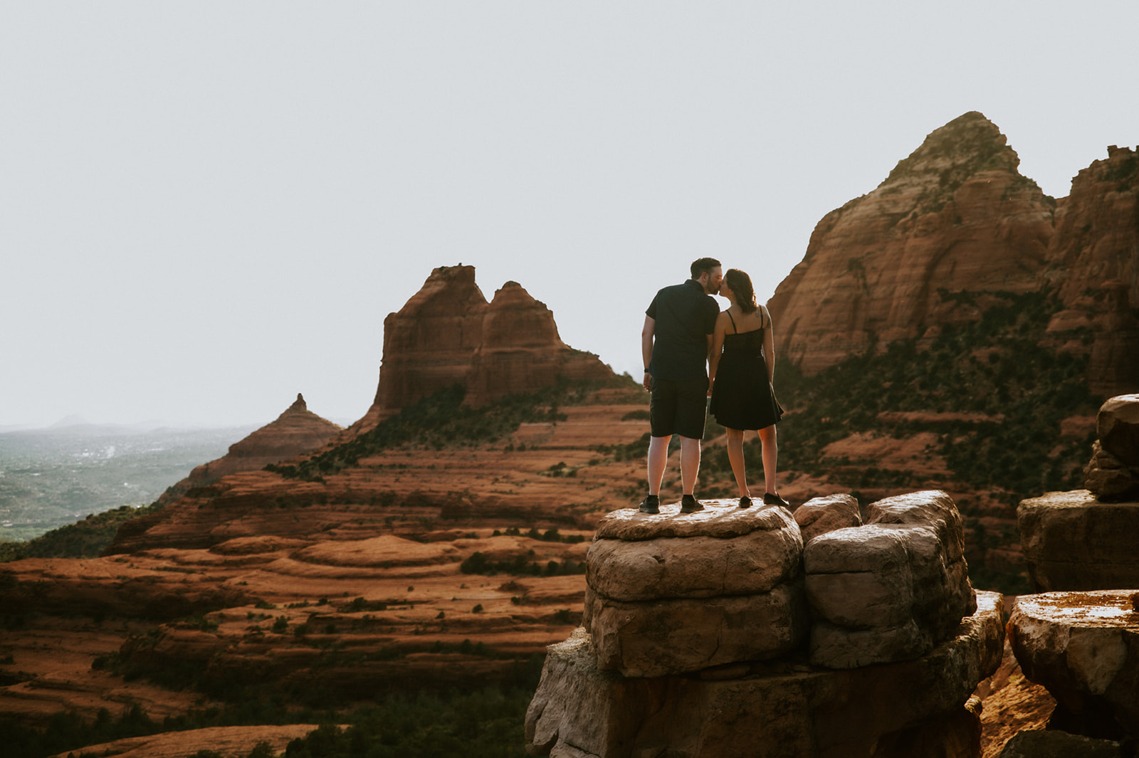Couple standing on a cliffside ledge taking in the layered red rock views after choosing to elope to Sedona