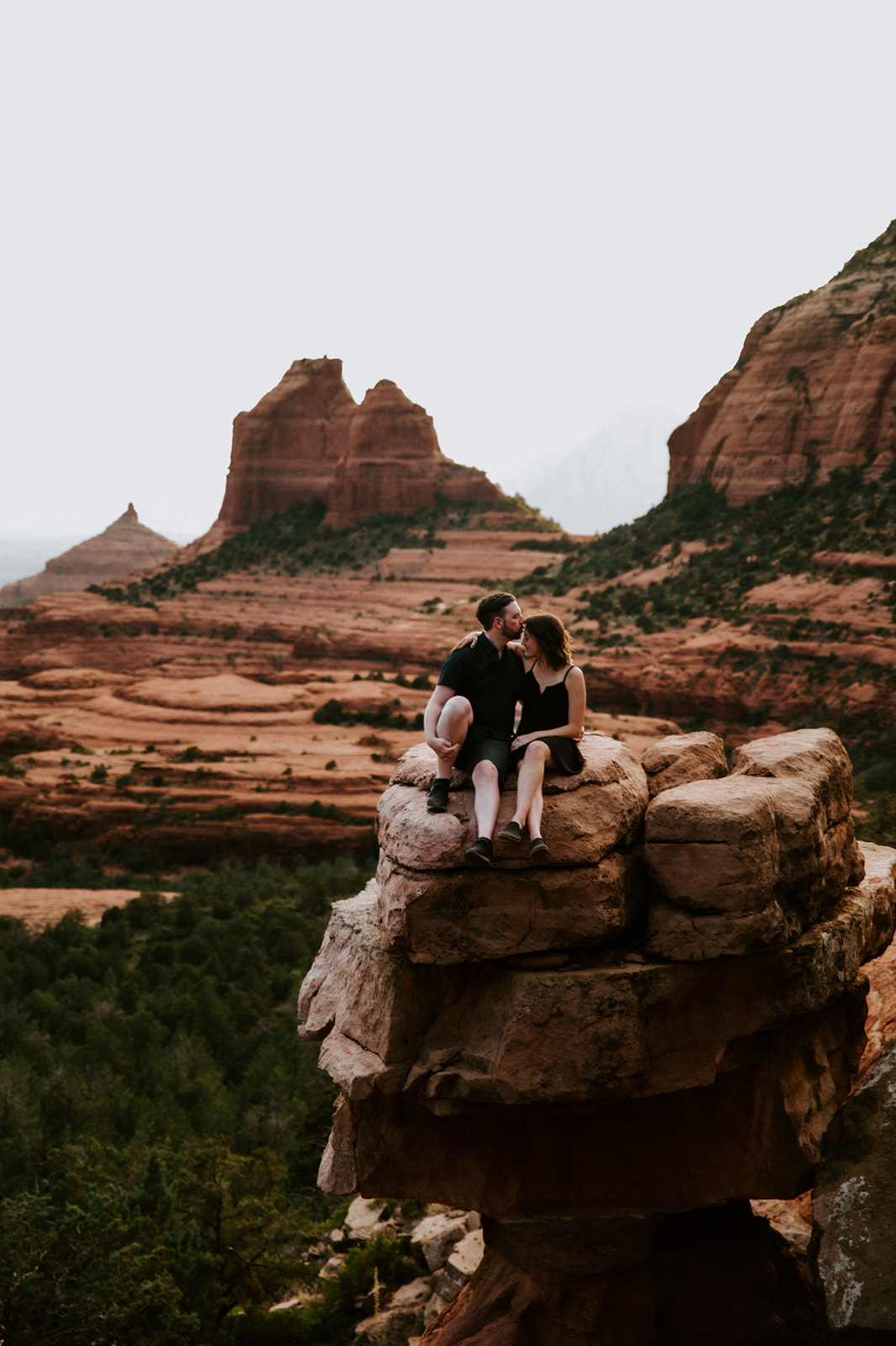 Couple sitting on a rock ledge overlooking Sedona’s red rock formations during an intimate moment together