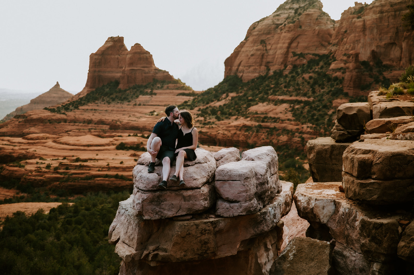 Couple sitting together on a cliffside rock ledge with expansive Sedona views behind them