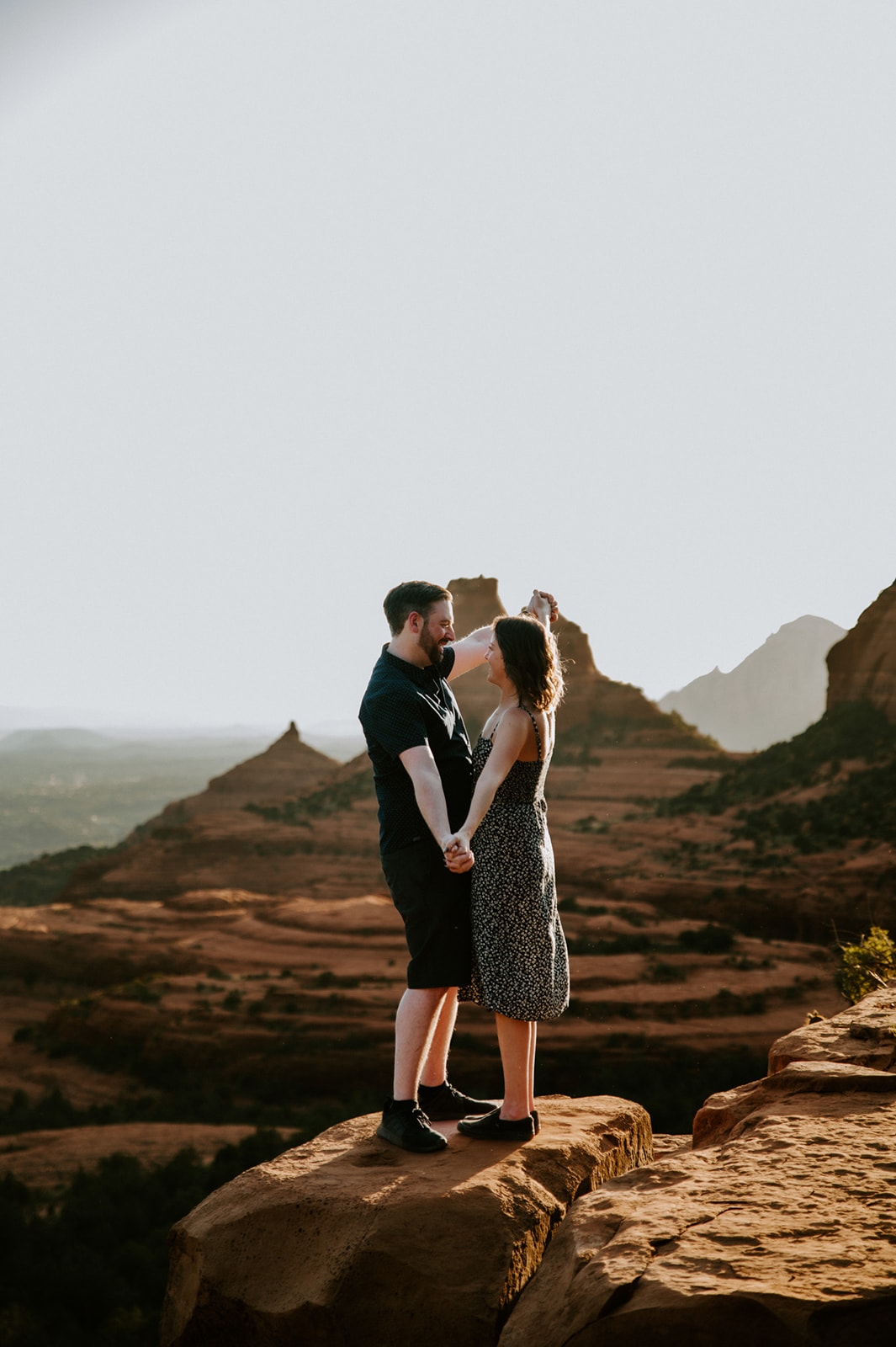 Couple holding hands on a cliffside overlook with layered red rock views after they elope to Sedona